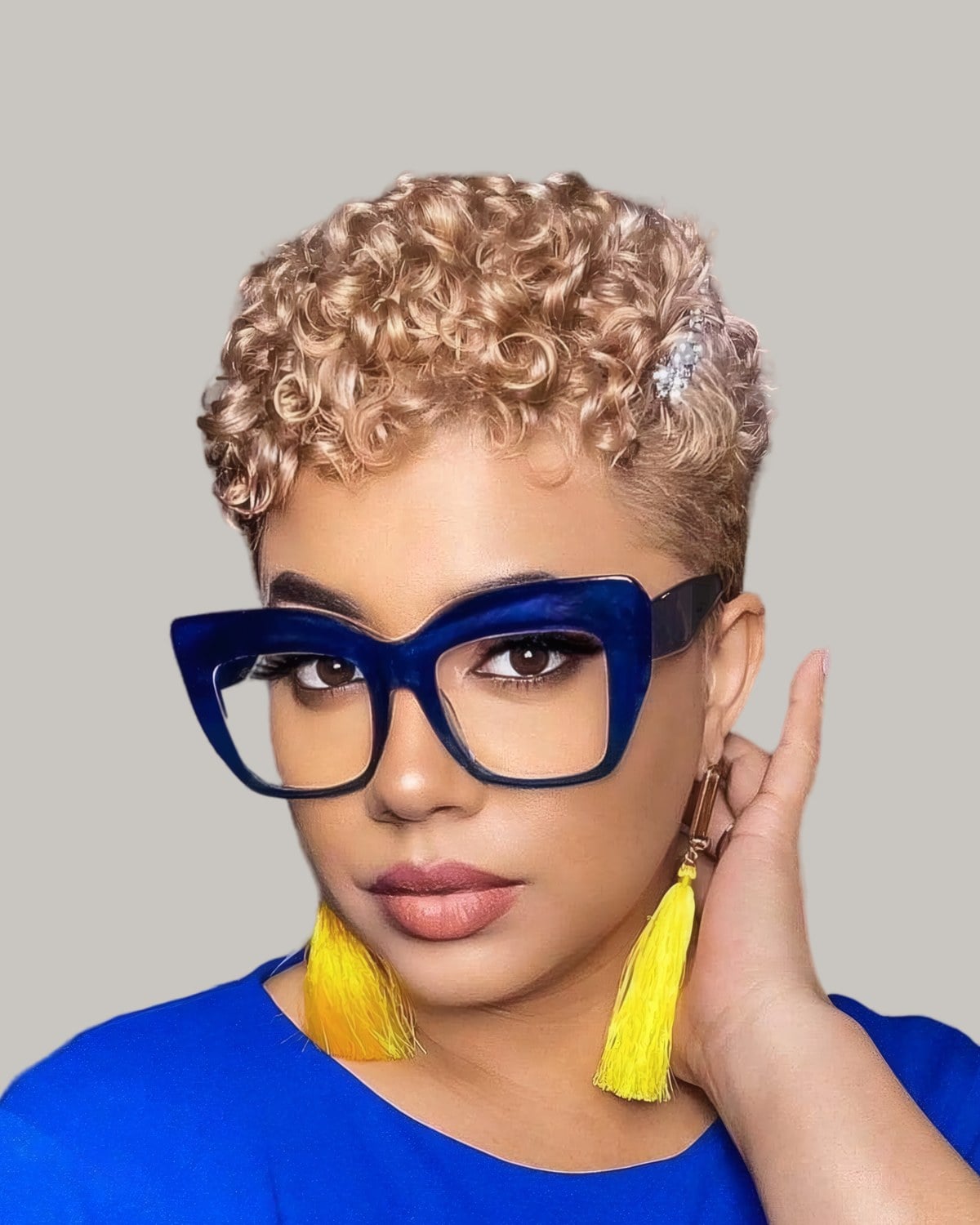 Woman with a short golden curly pixie, blue glasses and yellow tassel earrings