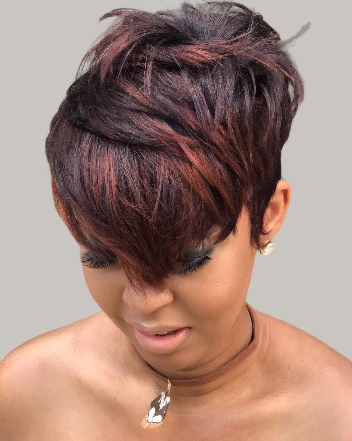 Woman with a reddish-brown layered pixie and a long fringe, looking down
