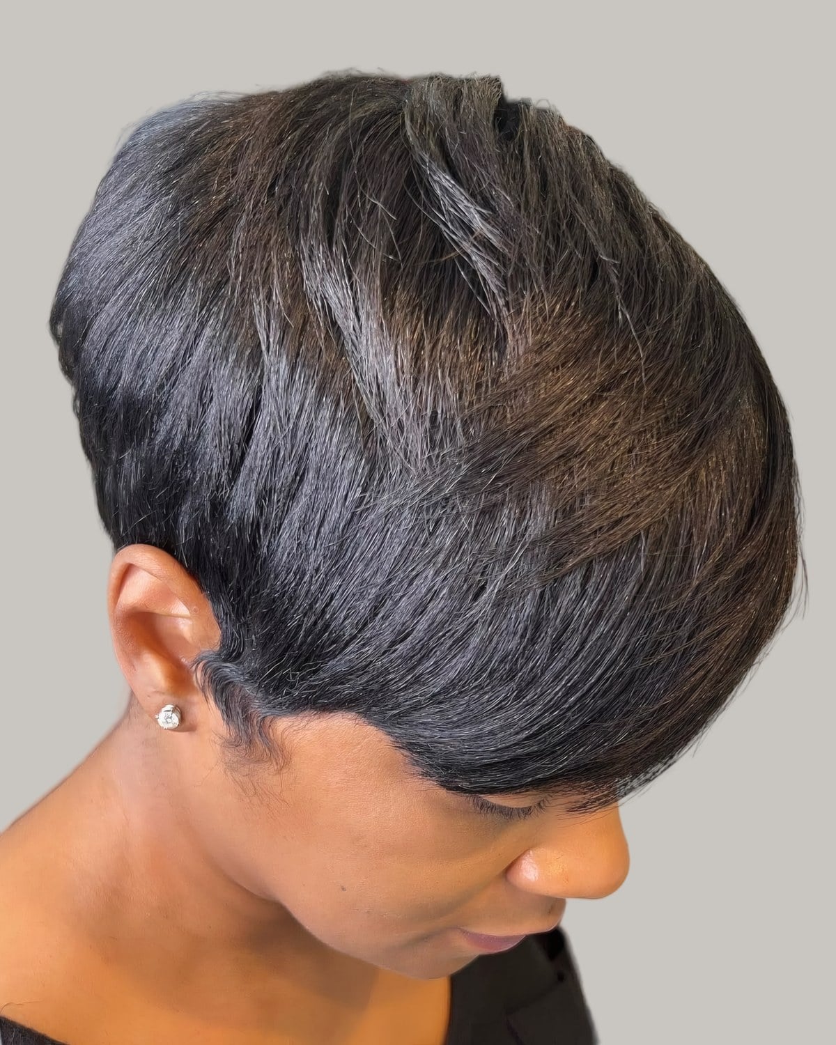 Woman with a glossy dark pixie seen from the side, looking down