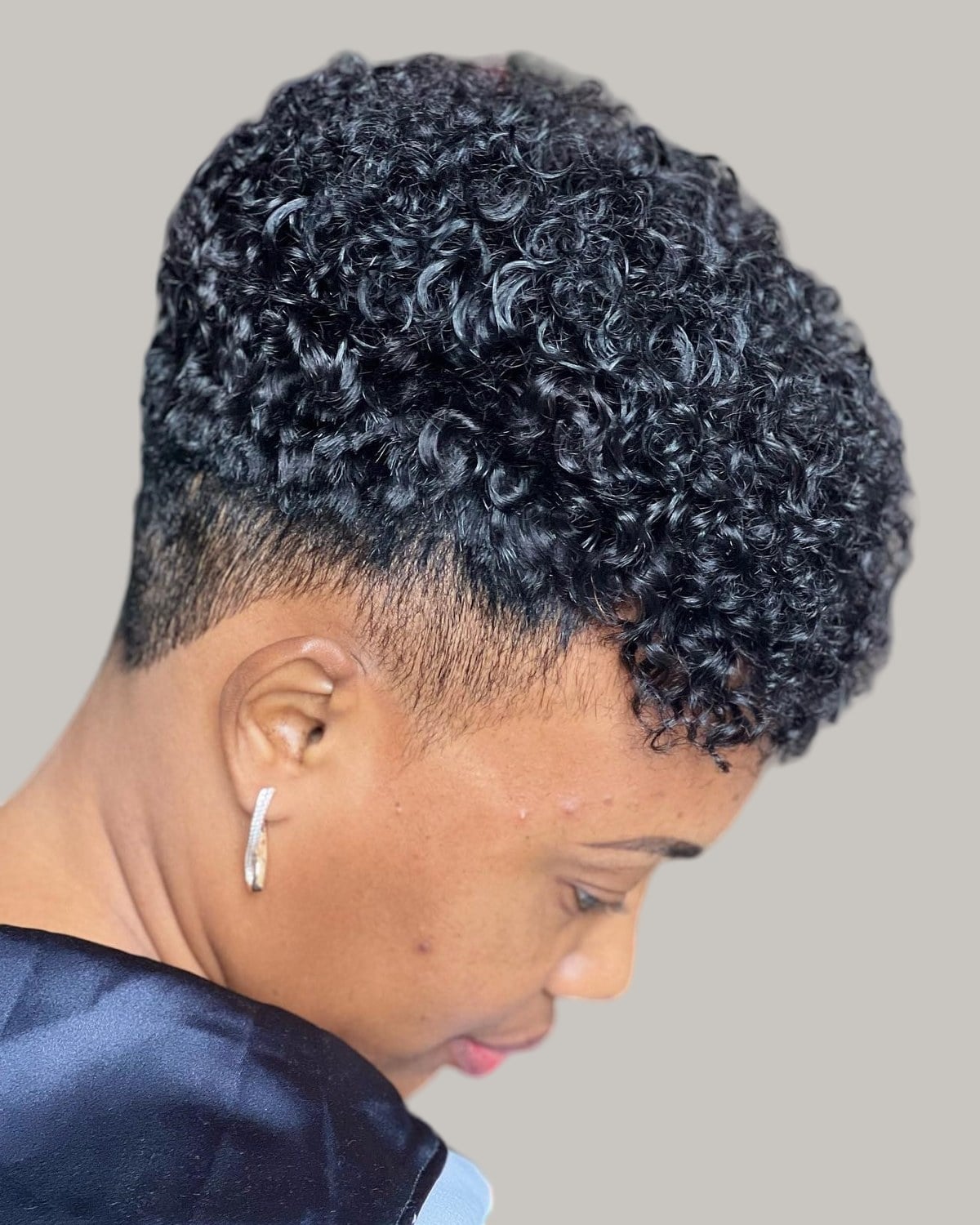 Woman with a tapered cut and short tight curls on top, seen from behind and to the side