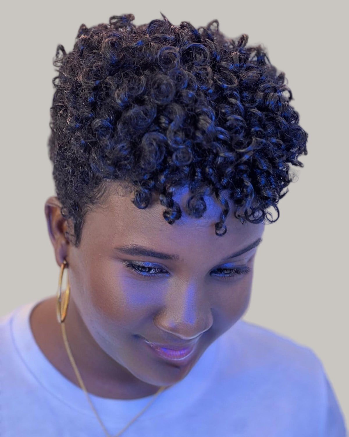 Woman with dark defined curls on top, lit in blue, looking down