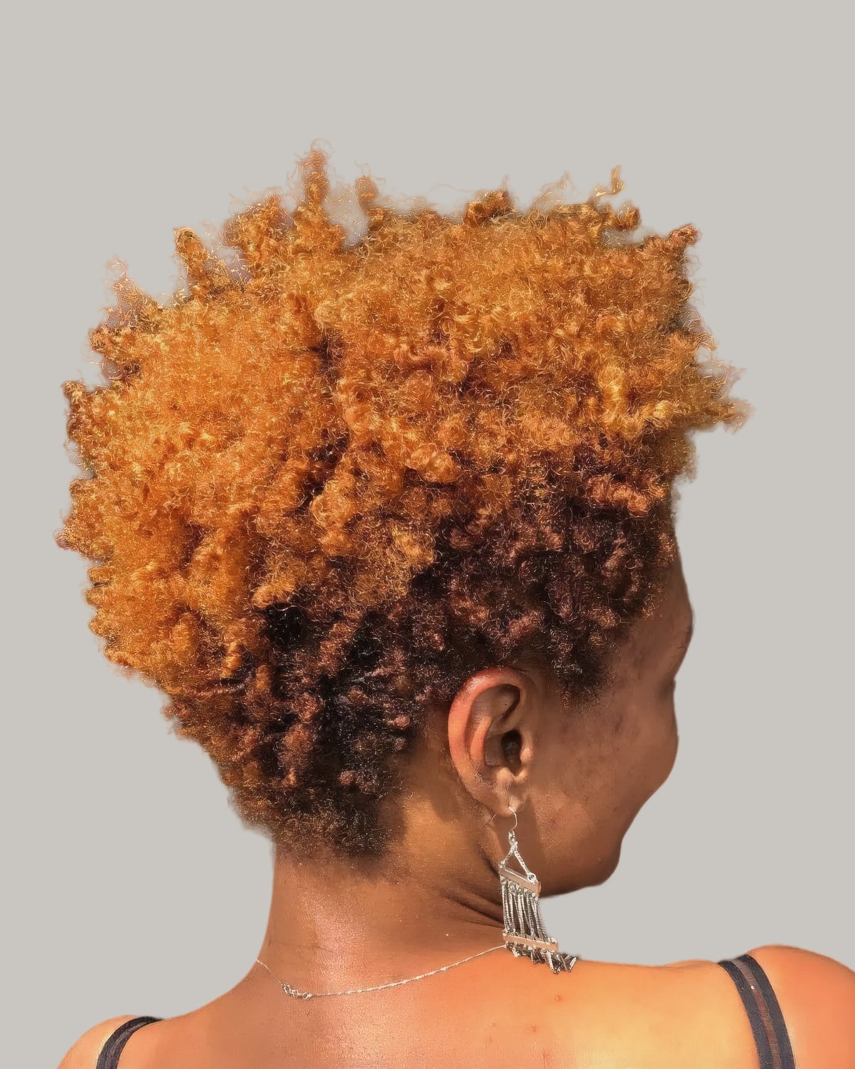 Woman with bright copper springy curls and a short taper, seen from the side