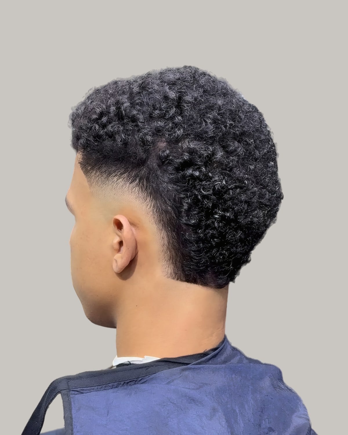 Man with a curly afro and a burst fade, seen from behind