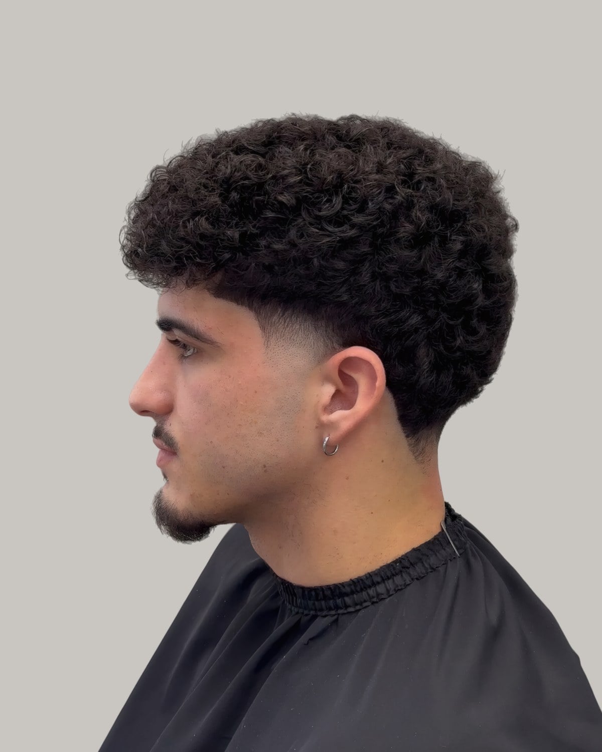 Man with curly hair, a light beard and a burst fade, seen at an angle
