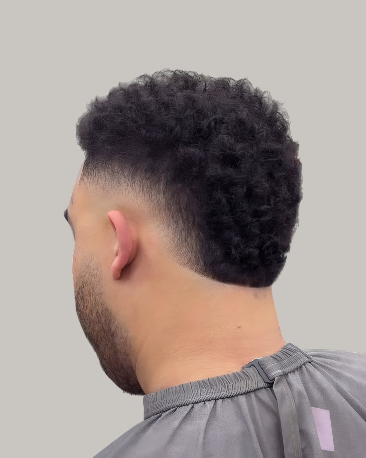 Bearded man with a curly top and a burst fade, seen from behind at an angle