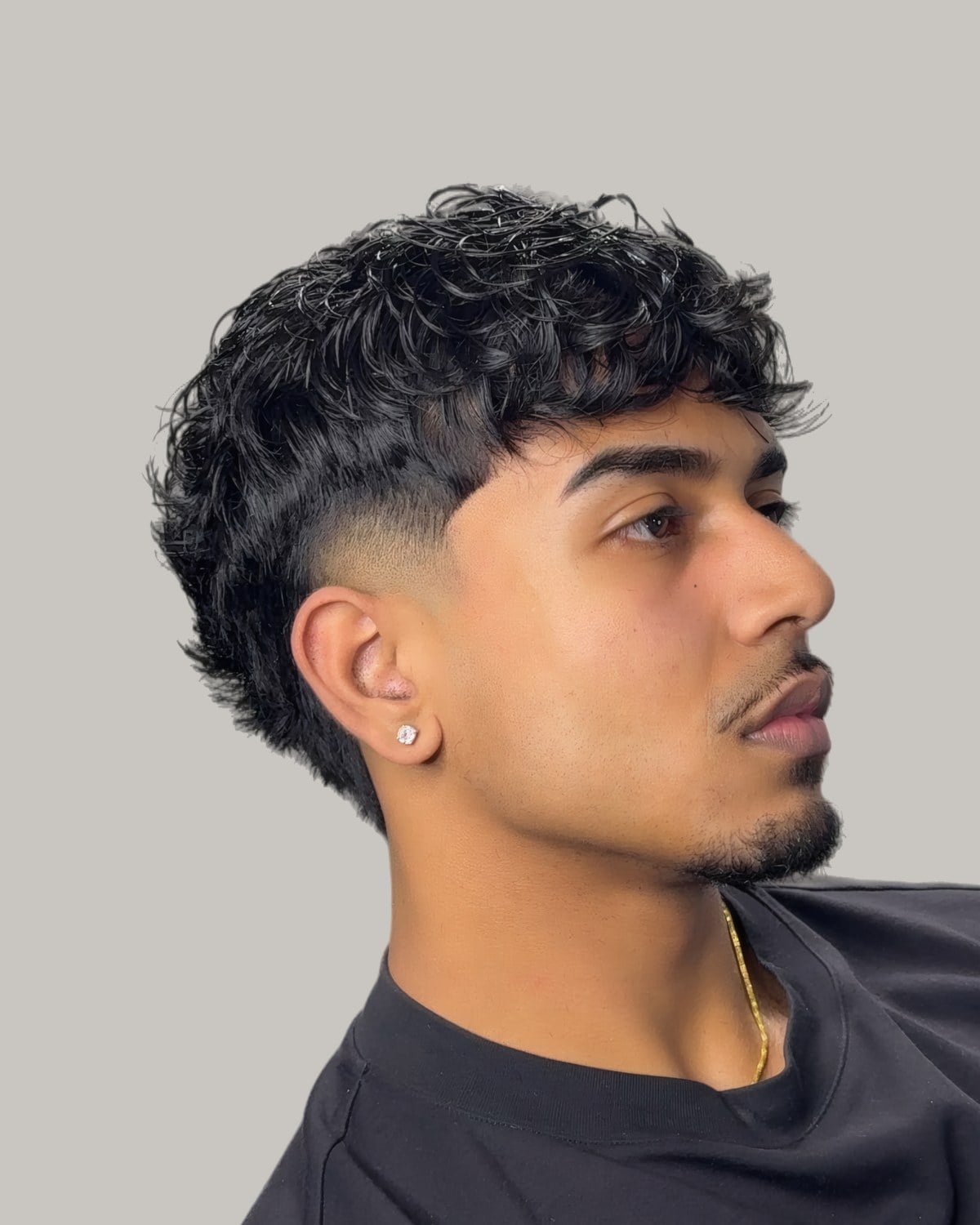 Man with a curly fringe and a burst fade, seen at an angle