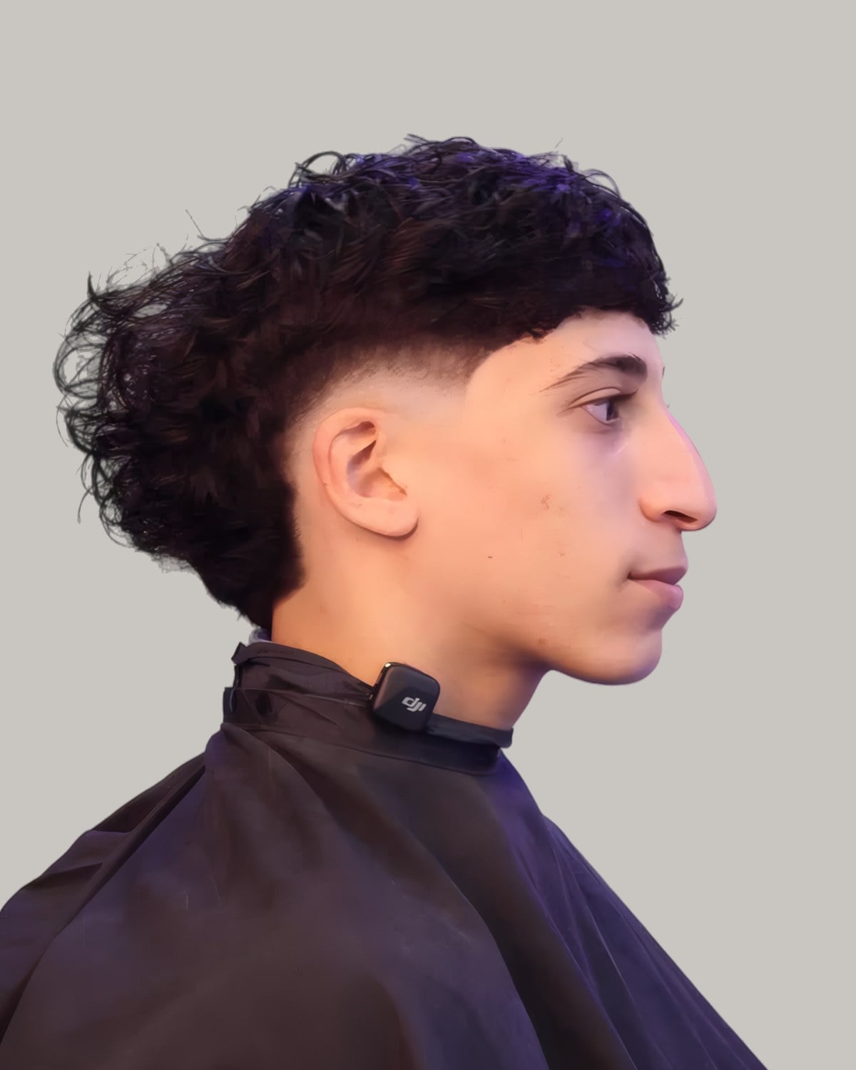Young man with a curly fringe falling onto his forehead and a burst fade, seen in profile