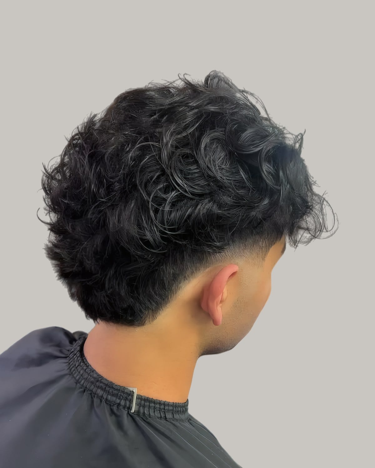 Man with a curly haircut and a burst fade, seen from behind at an angle