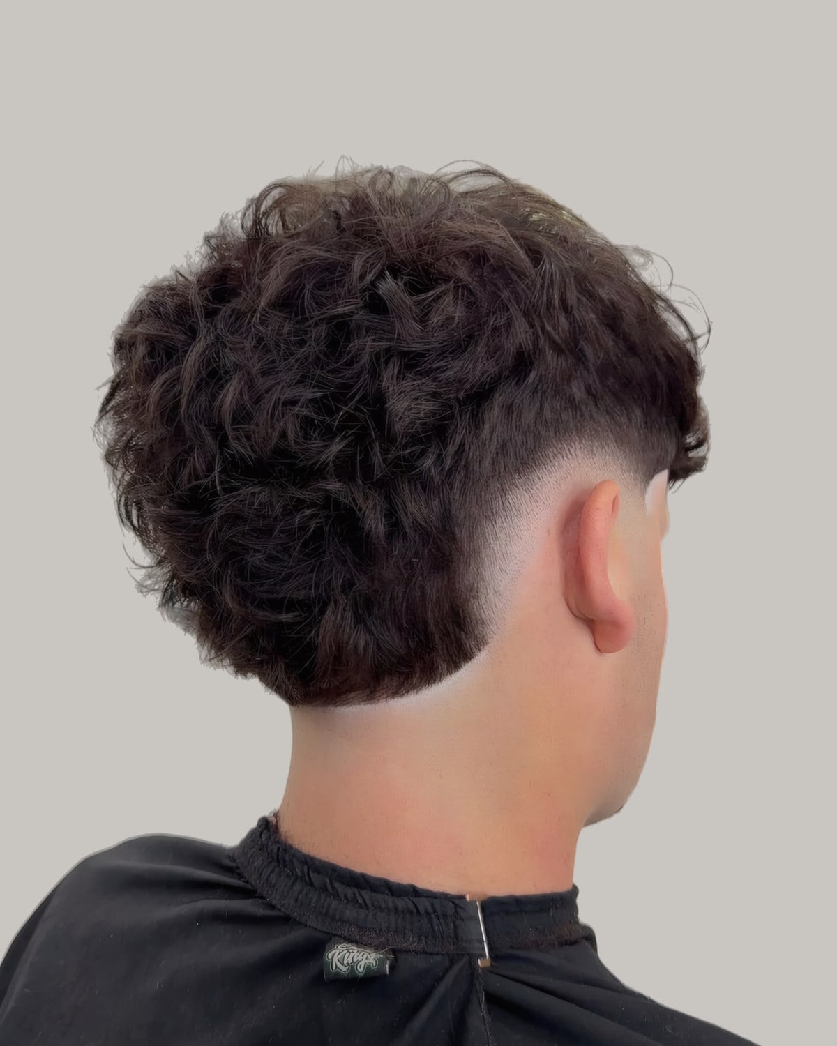 Man with a round curly haircut and a burst fade, seen from behind