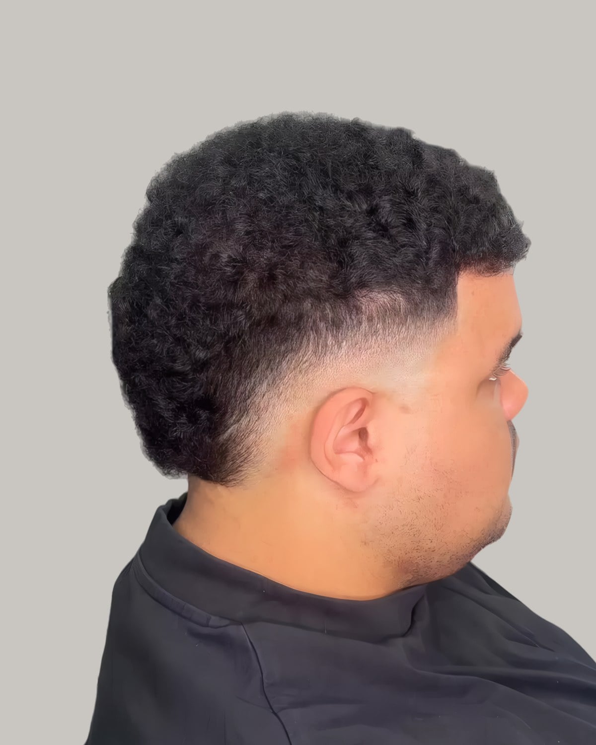 Man with short curly hair and a low burst fade, seen from the side