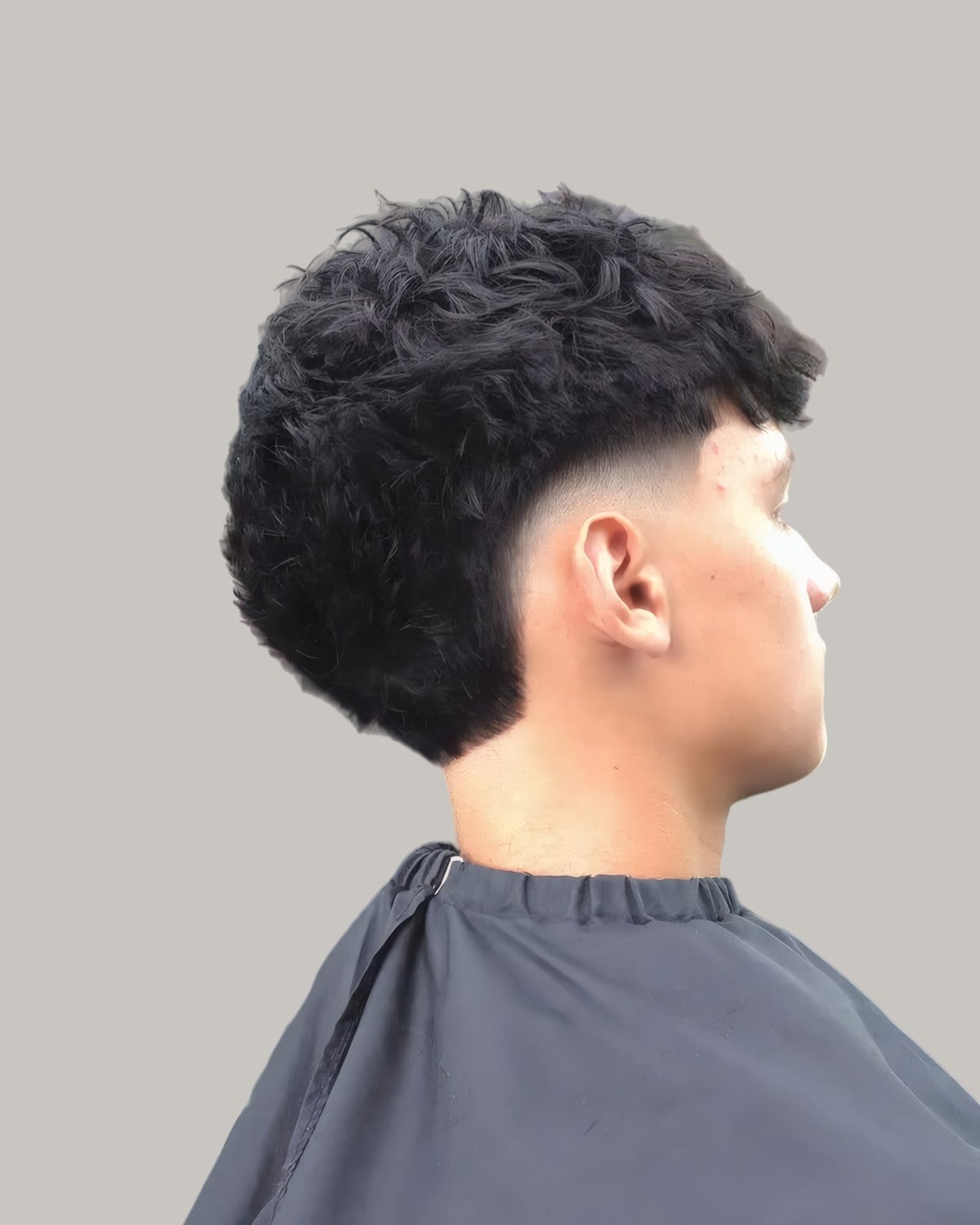 Man with a full curly top and a low burst fade, seen from the side