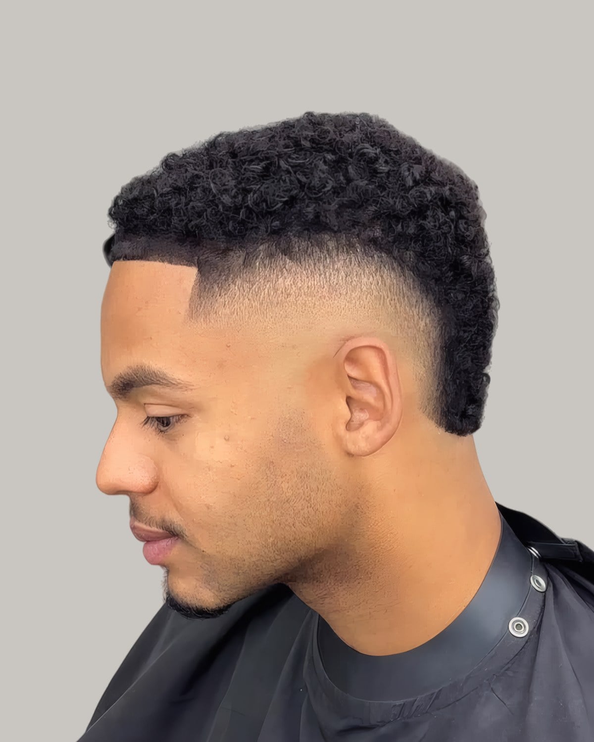 Man with a tight-curl mohawk, a burst fade and a sharp hairline, seen at an angle
