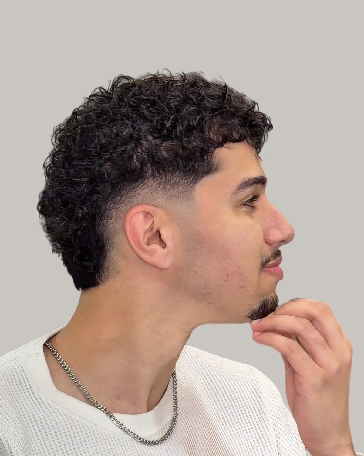 Man with a curly mohawk and a burst fade, seen in profile