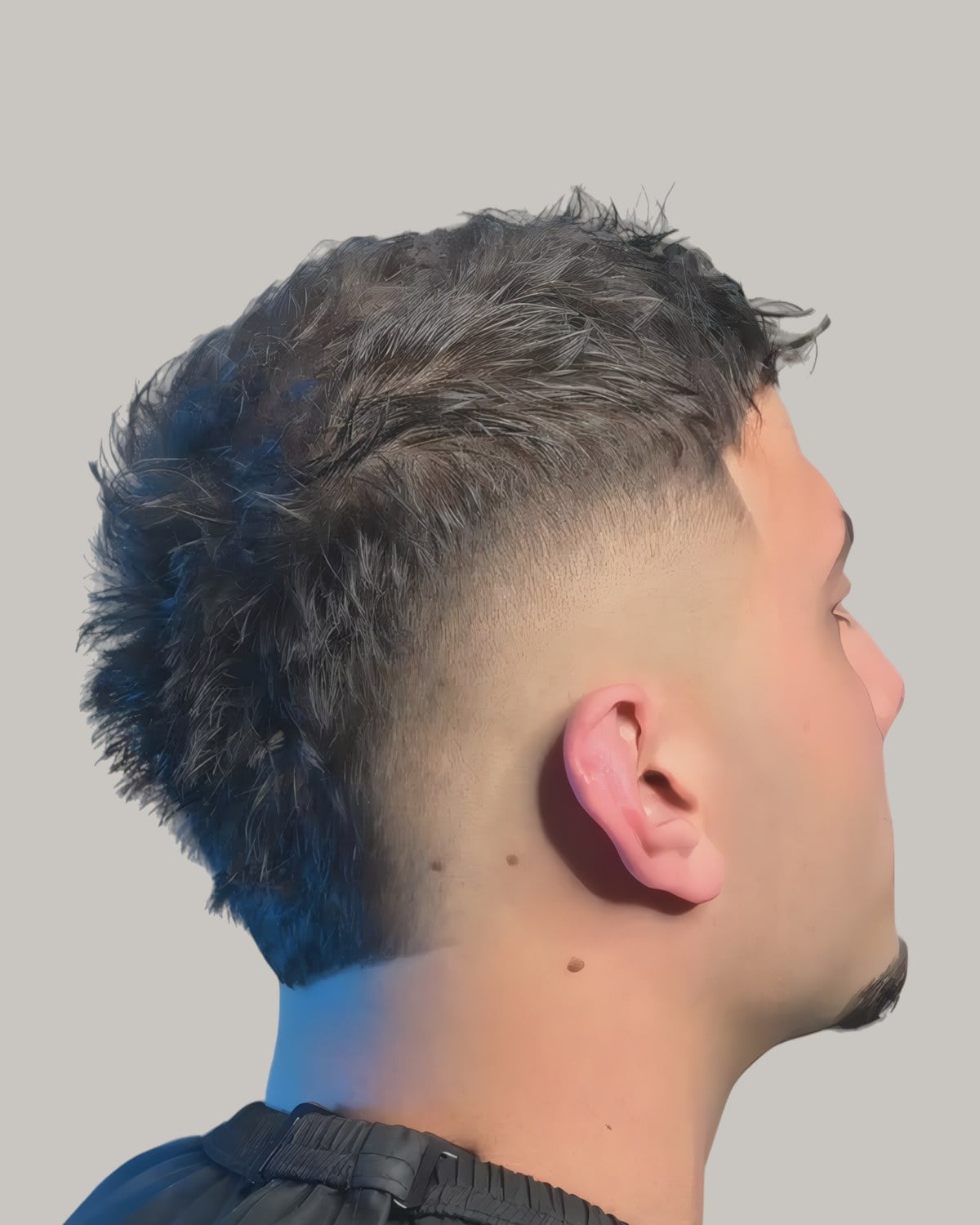 Man with a dark spiky faux hawk and a burst fade, seen in profile
