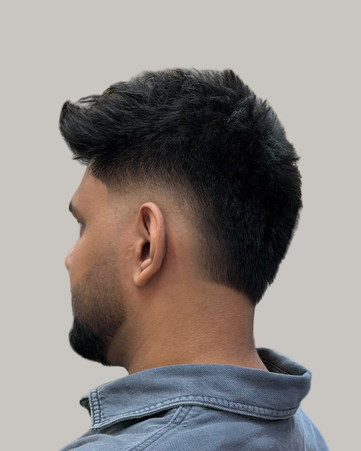 Bearded man with a black spiky faux hawk and a burst fade, seen from behind at an angle