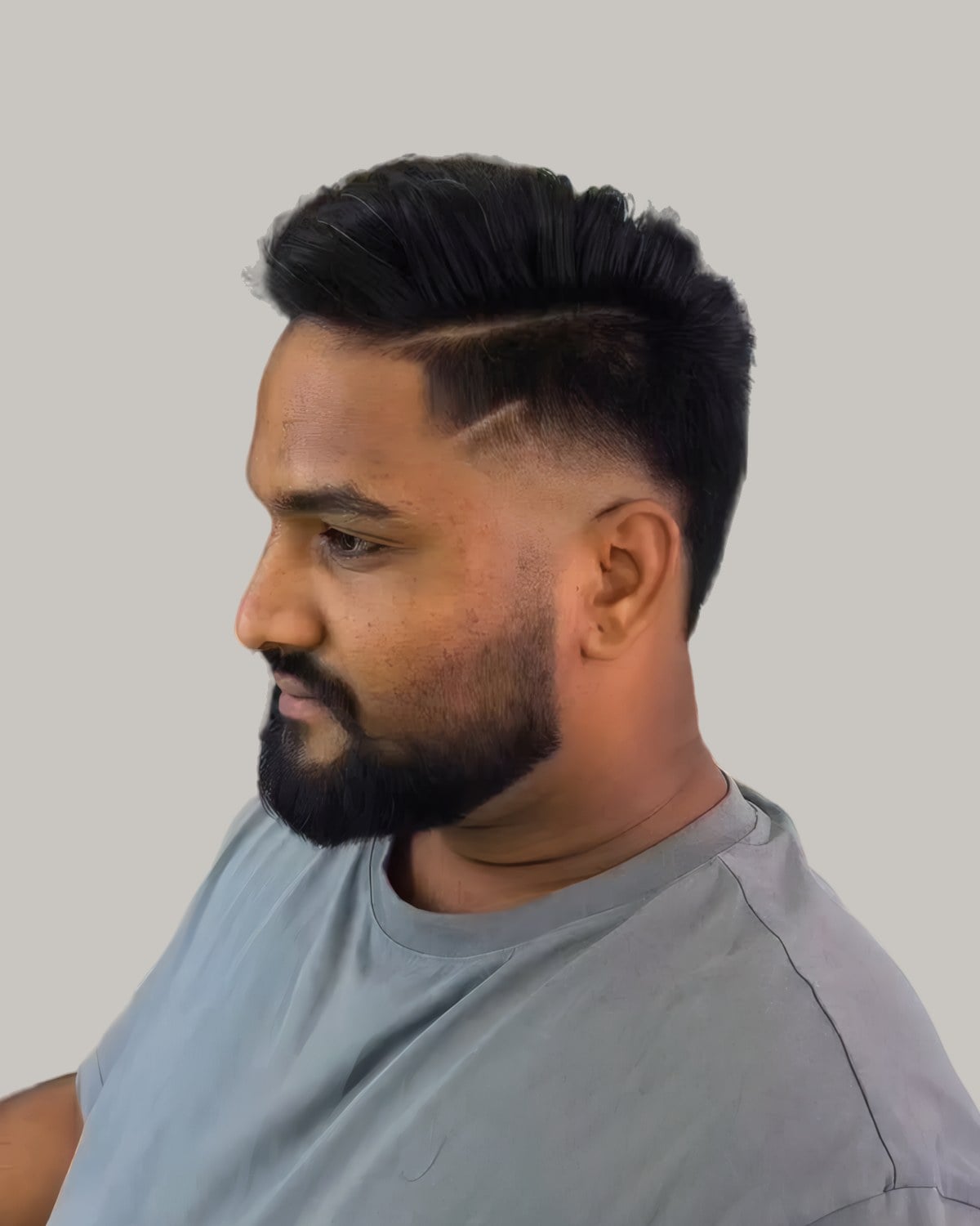 Bearded man with a combed-back dark top, a shaved part and a burst fade, seen at an angle