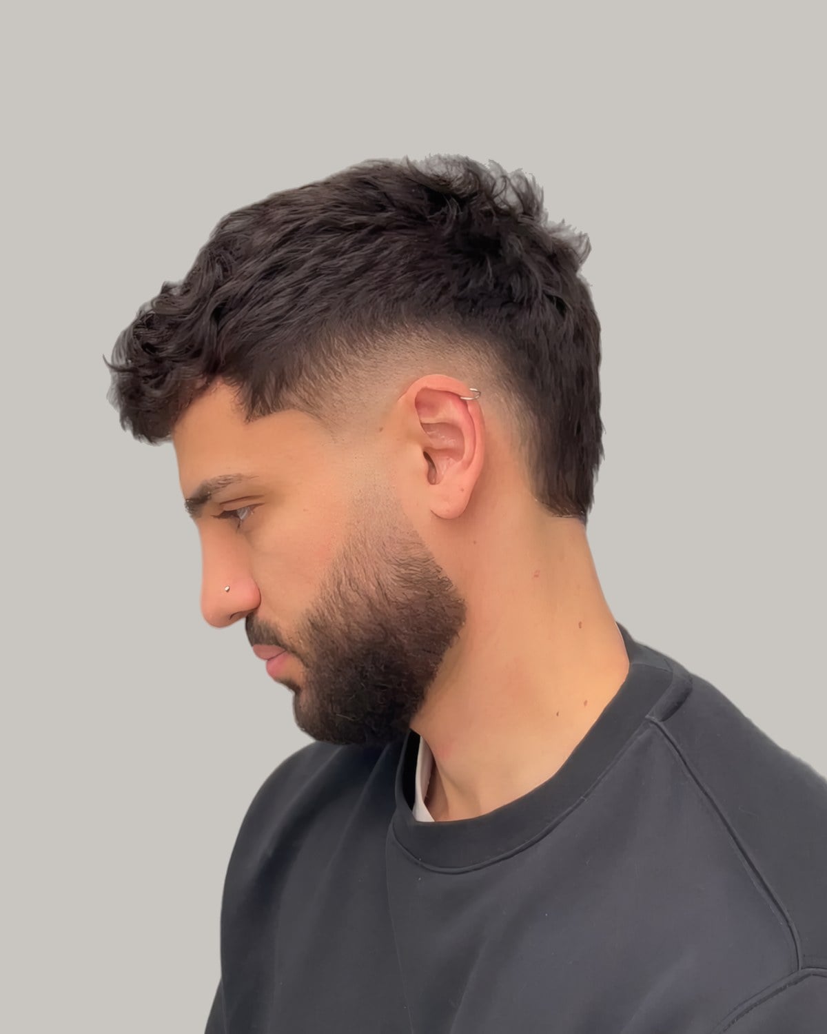 Bearded man with a textured dark top and a burst fade, looking down