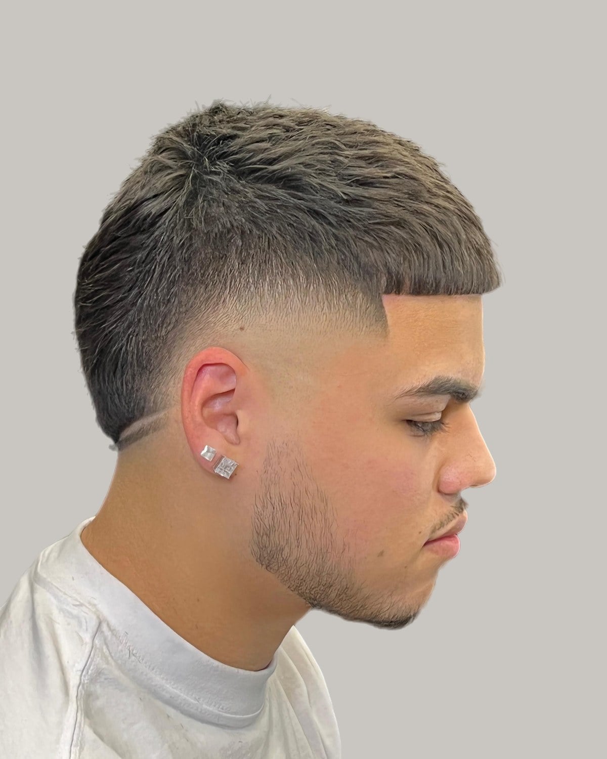 Man with a short textured crop, a shaved line and a high burst fade, seen at an angle