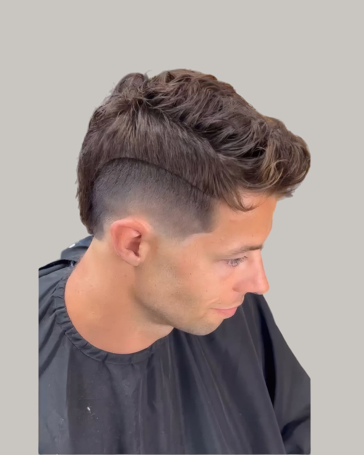 Man with a textured brown top, a hard part and a high burst fade, looking down
