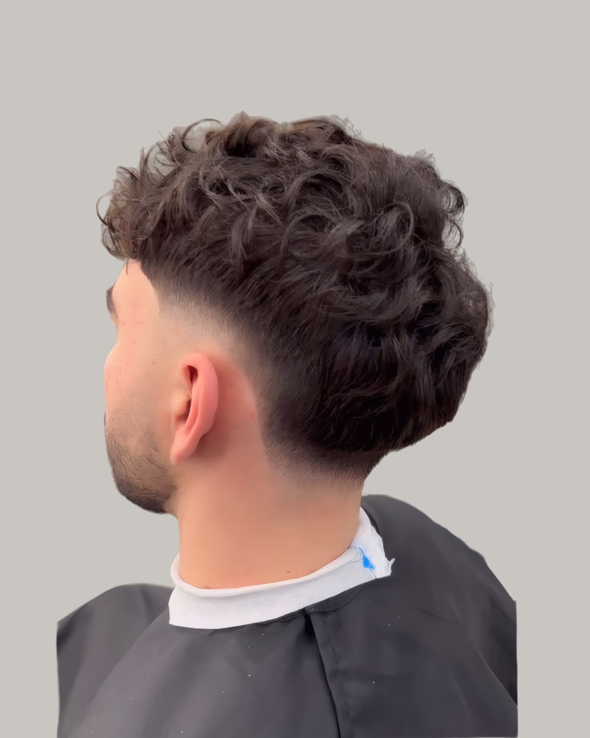 Man with loose brown curls and a burst fade, seen from behind at an angle