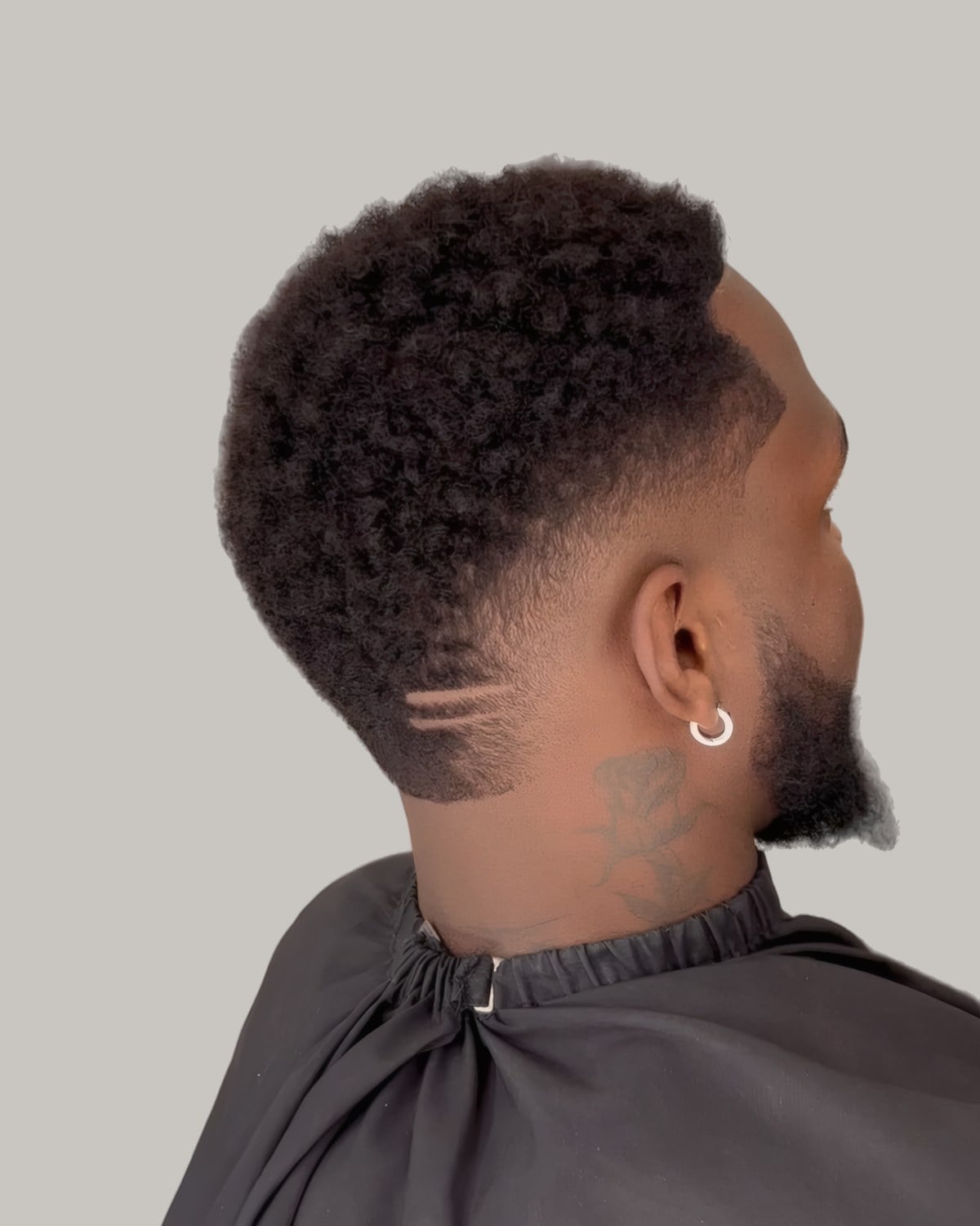 Man with short curly hair and a burst fade with shaved lines, seen from behind at an angle