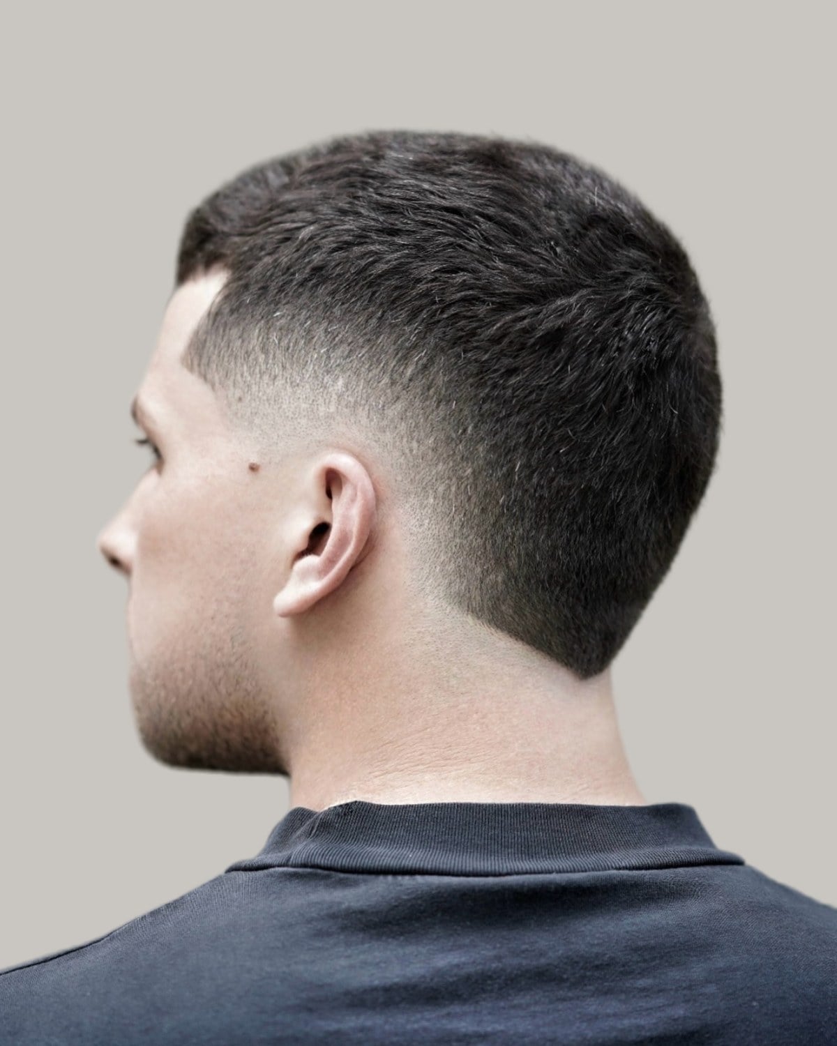 Man with short straight dark hair and a low burst fade, seen from behind at an angle