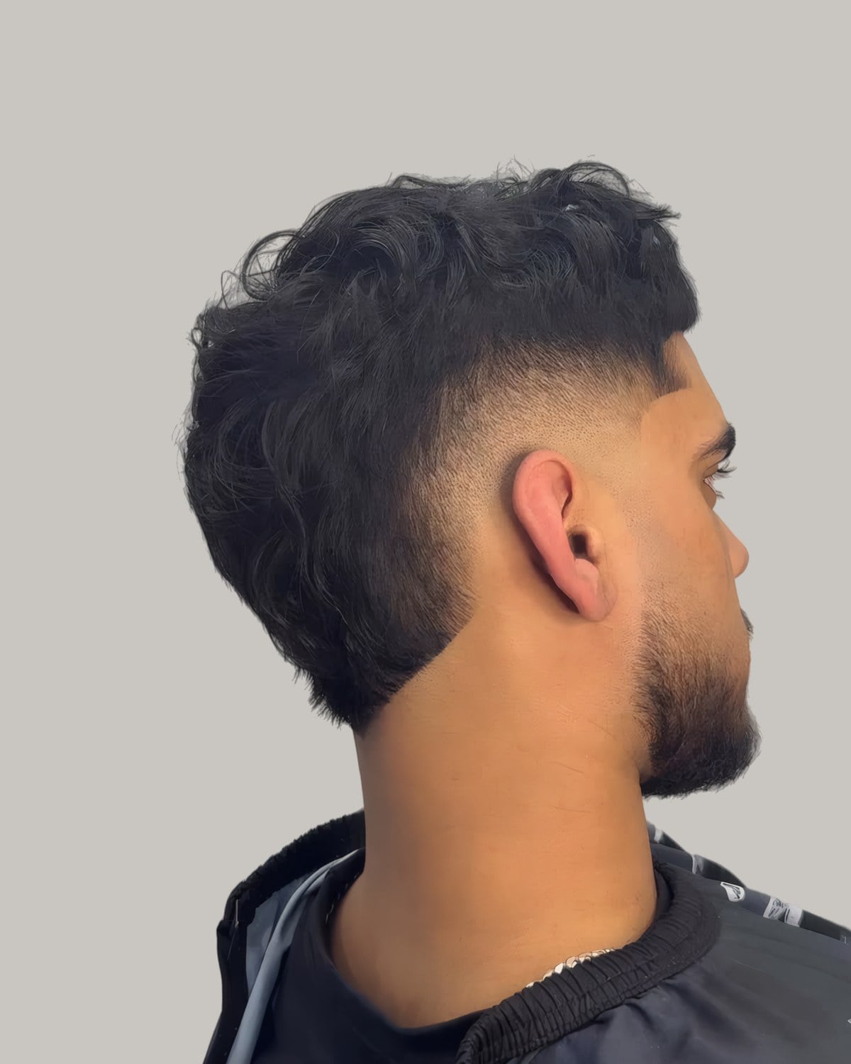 Bearded man with a wavy dark top and a low burst taper, seen from behind at an angle