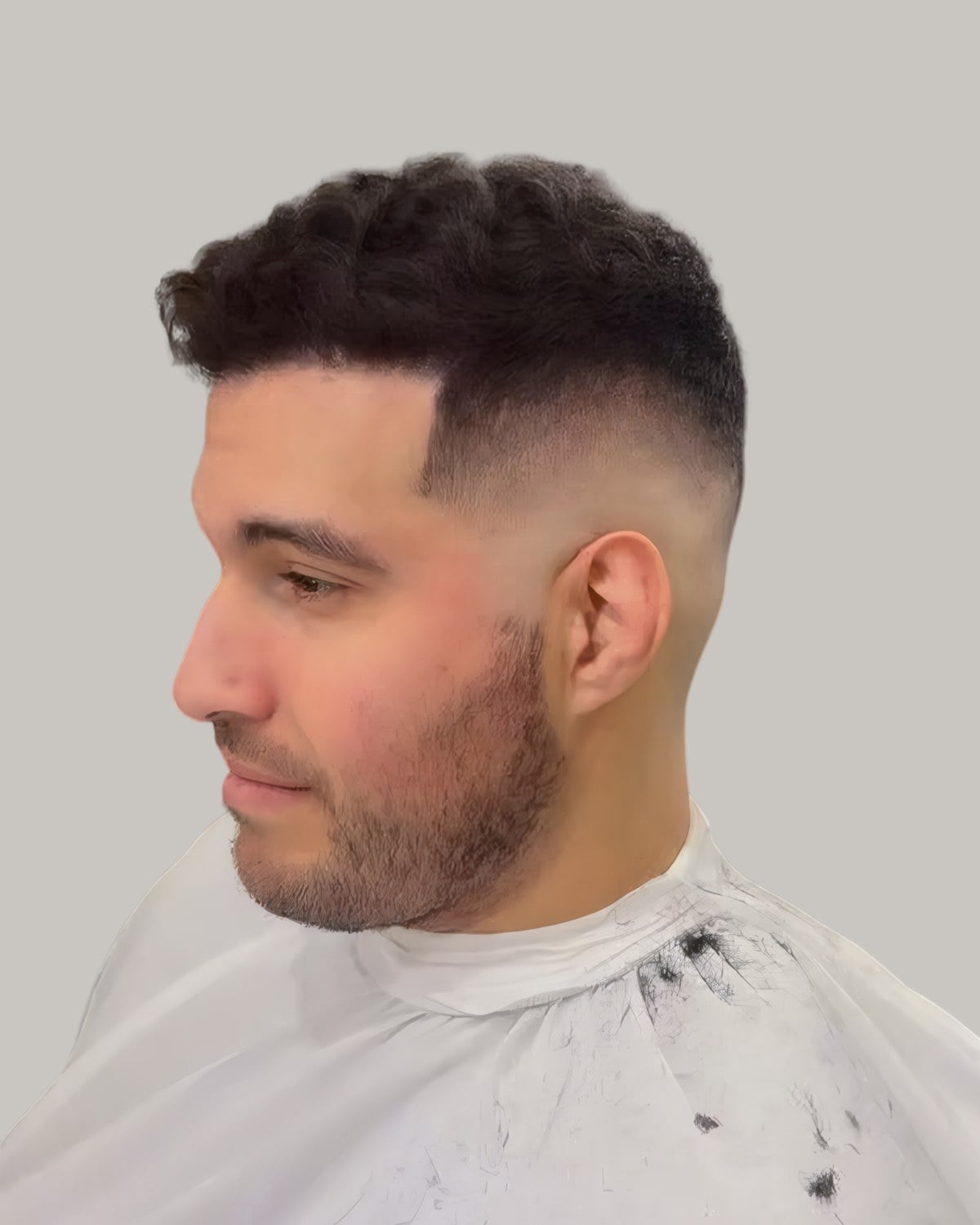 Man with a short textured fringe and a burst fade, looking down