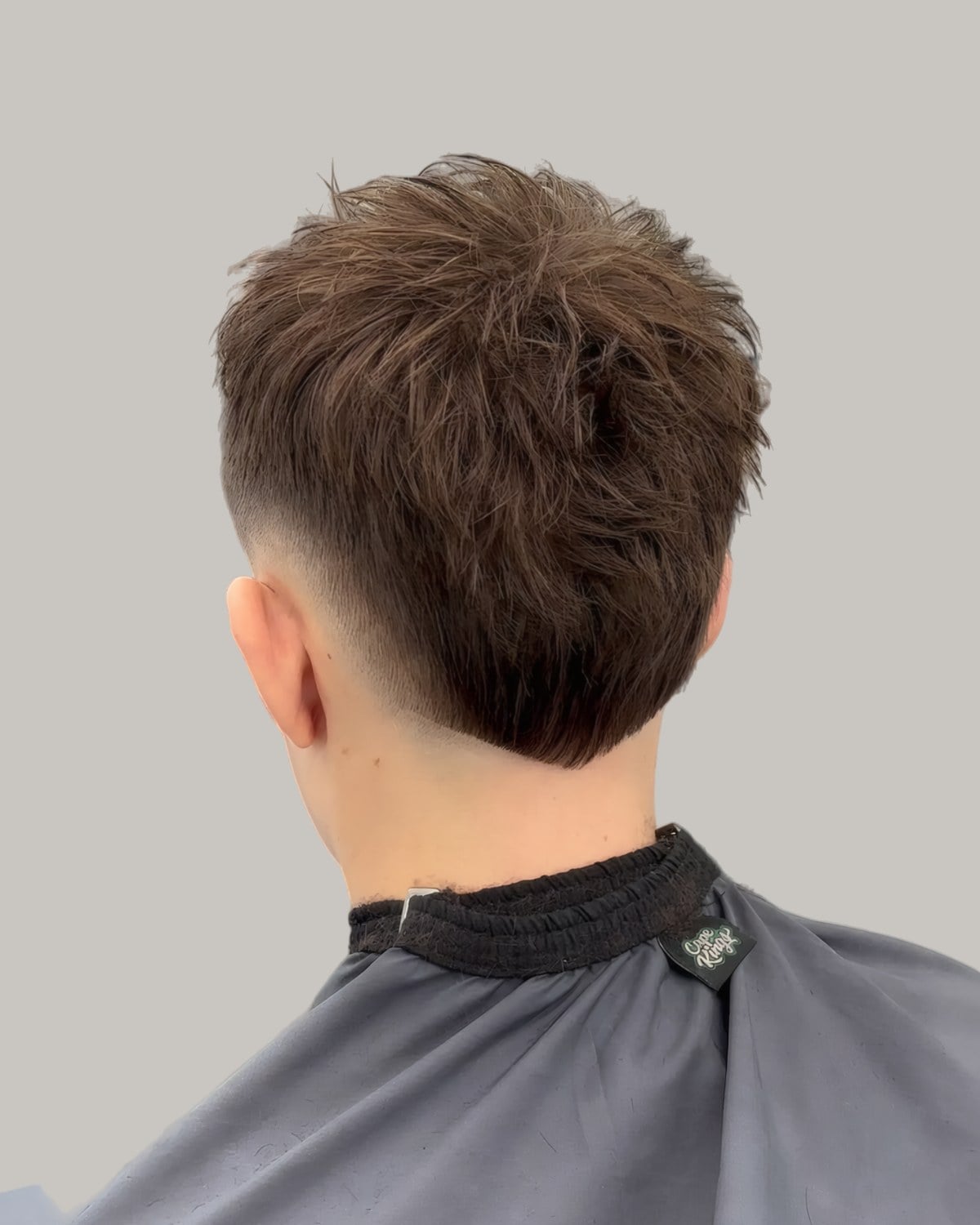 Man with a brown textured haircut and a mid burst fade, seen from behind