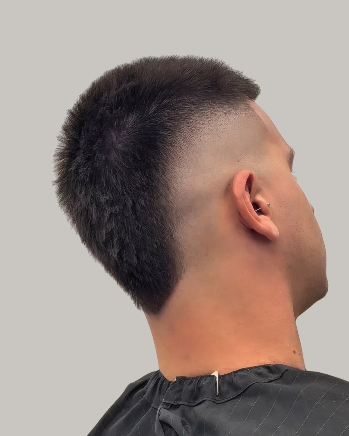 Man with a short dark mohawk and a high burst fade, seen from behind at an angle