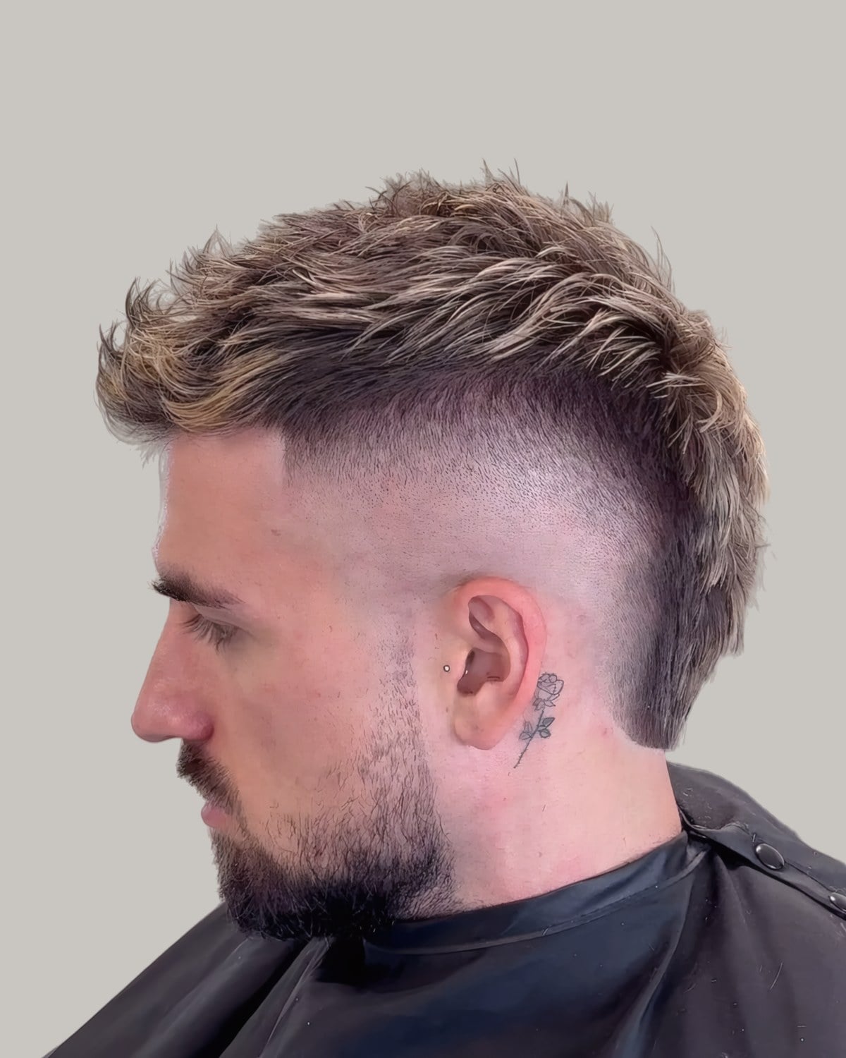 Bearded man with a blond-tipped textured mohawk and a skin fade, seen in profile