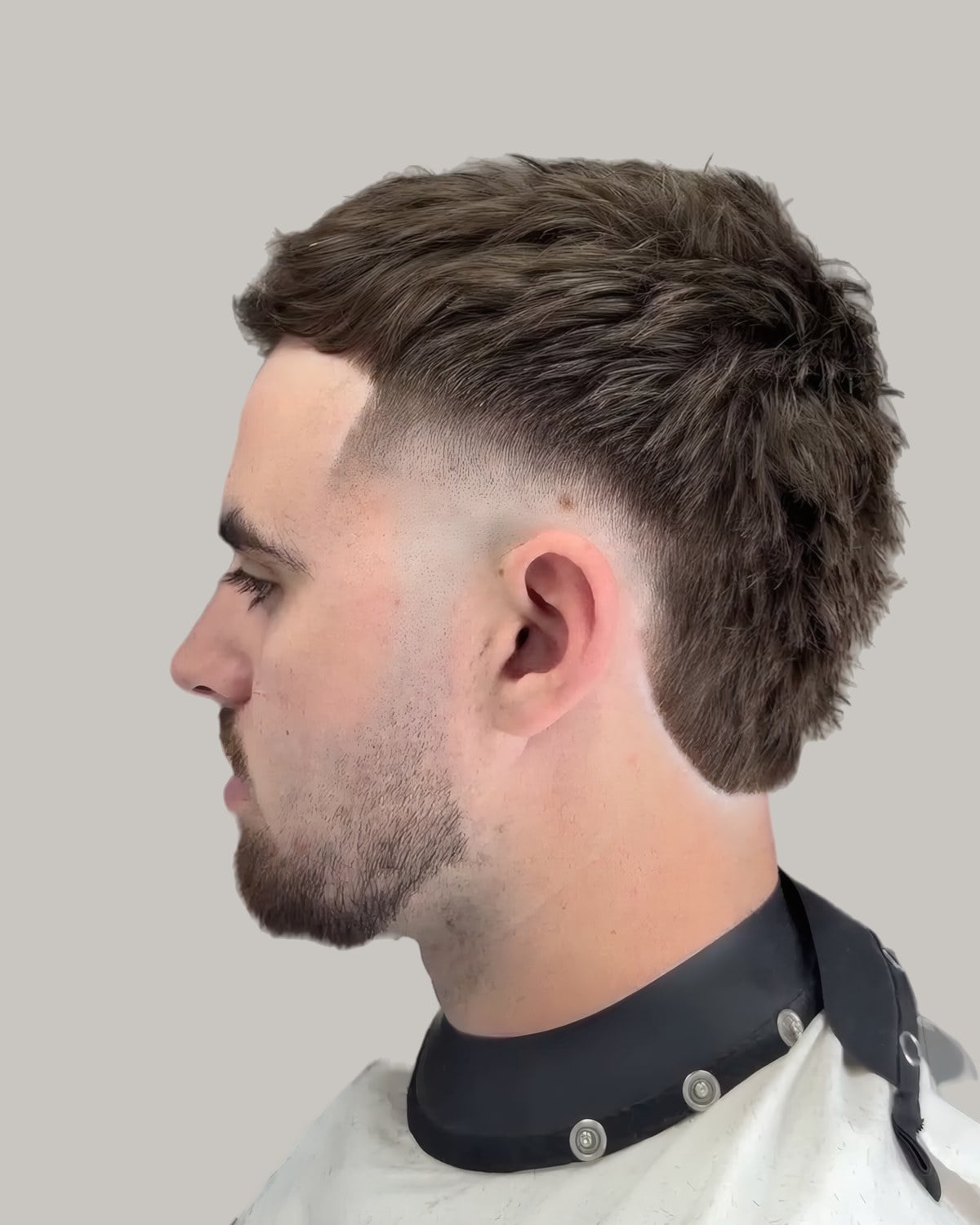 Man with a textured brown mullet and a trimmed beard, seen at an angle
