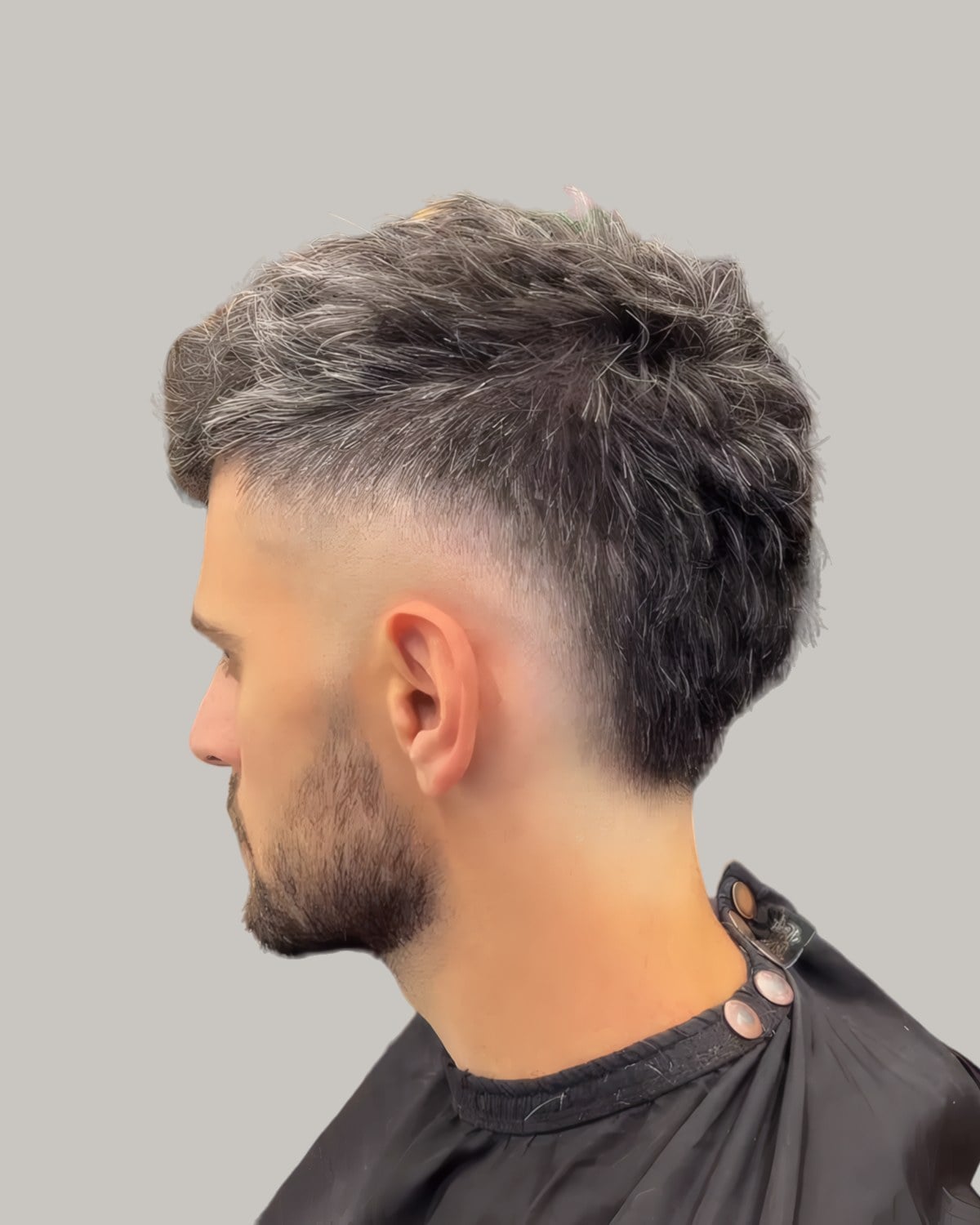 Bearded man with a spiky, grey-streaked mullet and a burst fade, seen from behind at an angle