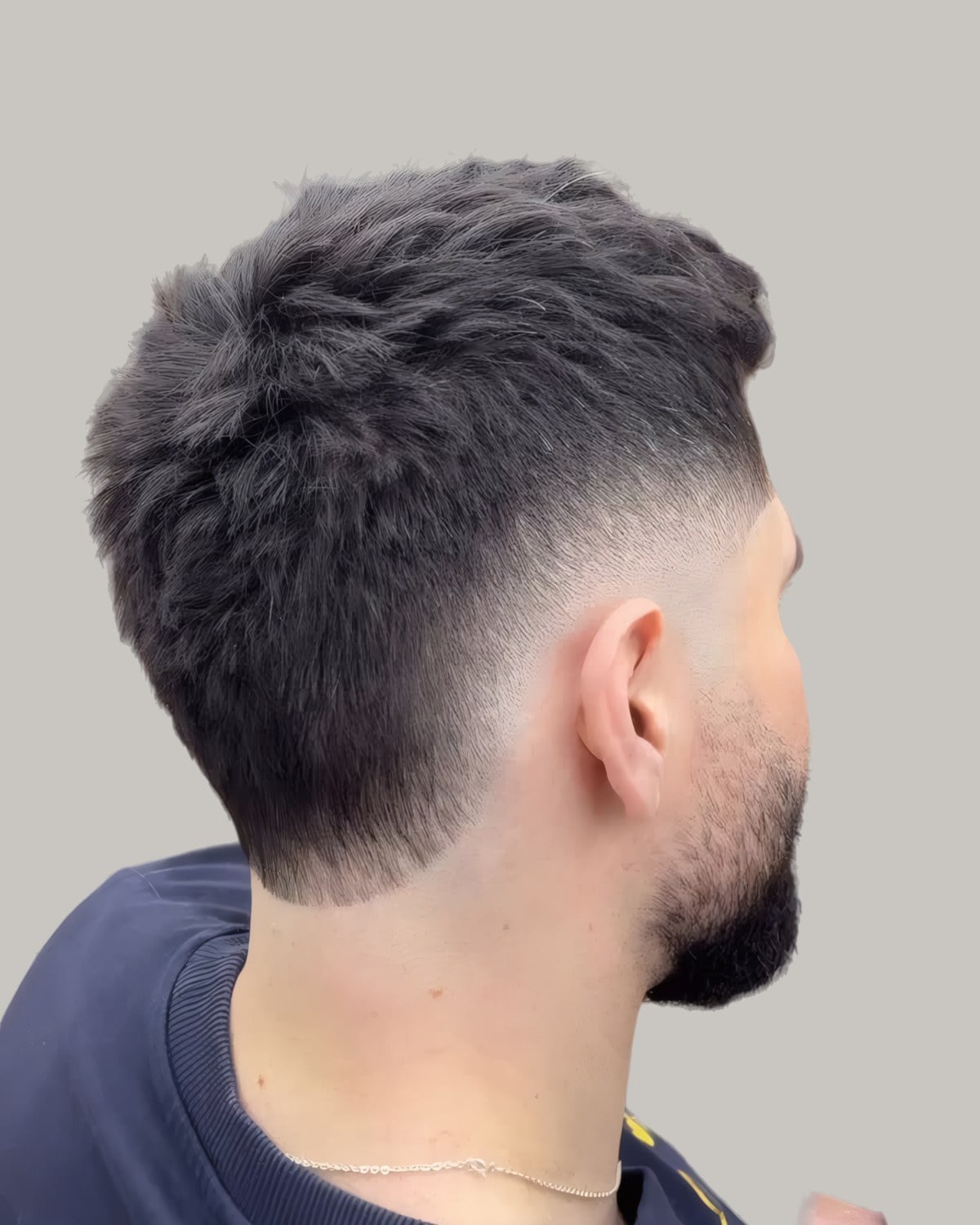 Man with a textured top, a short beard and a burst fade, seen from behind at an angle