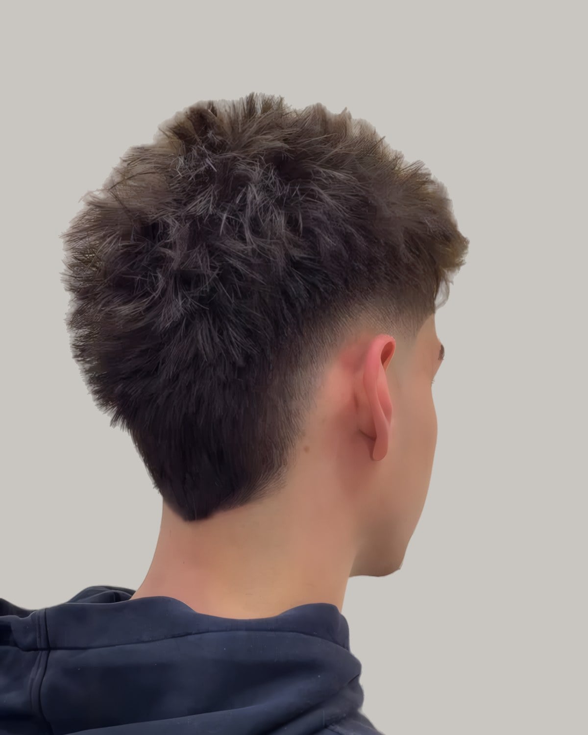 Man with short spiky hair and a burst fade, seen from behind at an angle