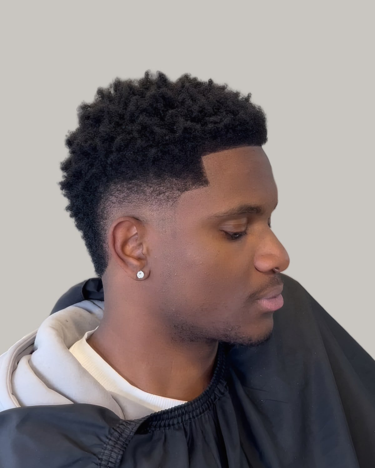 Man with short coils, a line-up and a burst fade, seen at an angle