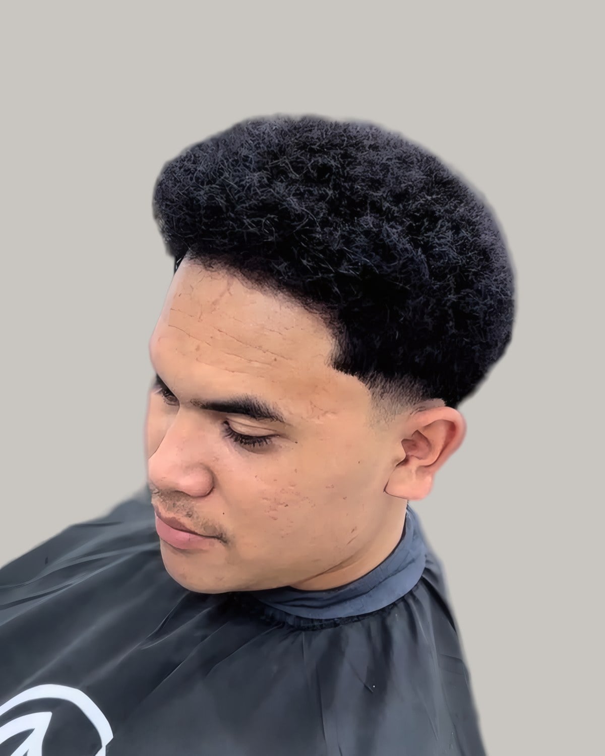 Young man with a short rounded afro and a burst fade, looking down