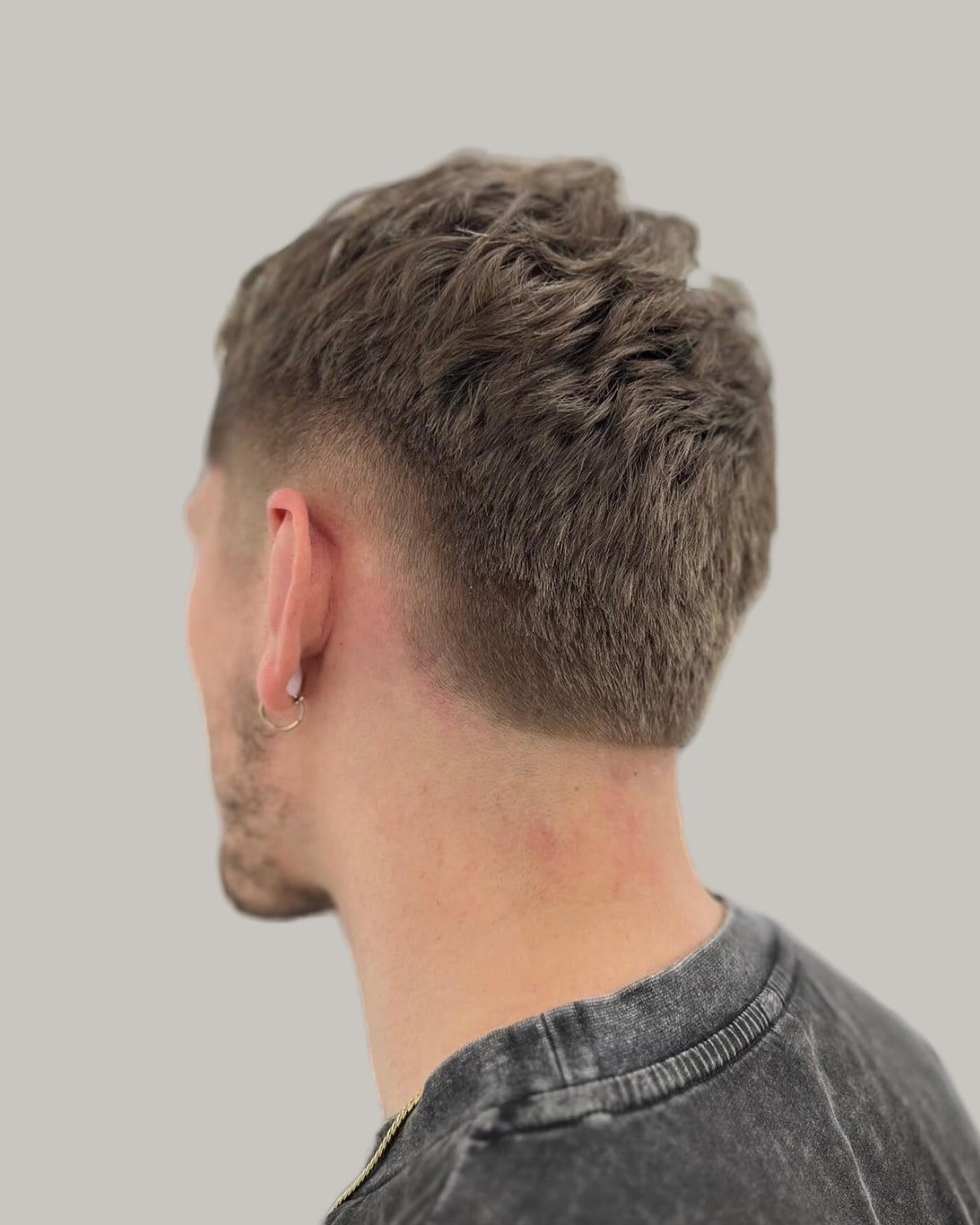 Man with a short brown textured haircut and a burst taper, seen from behind at an angle