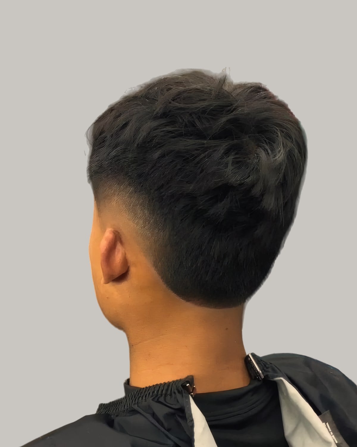 Man with a dark textured crop and a burst fade, seen from behind at an angle