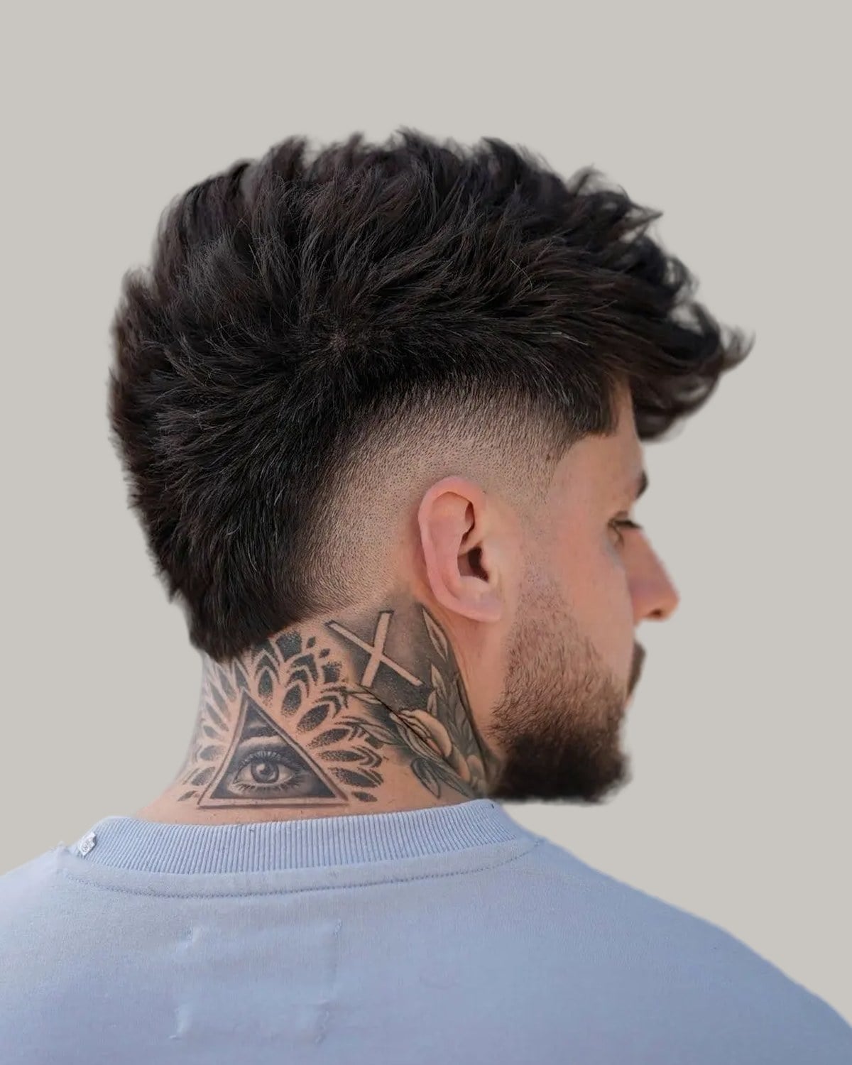Bearded man with a full dark textured top and a mid burst fade, seen from behind at an angle