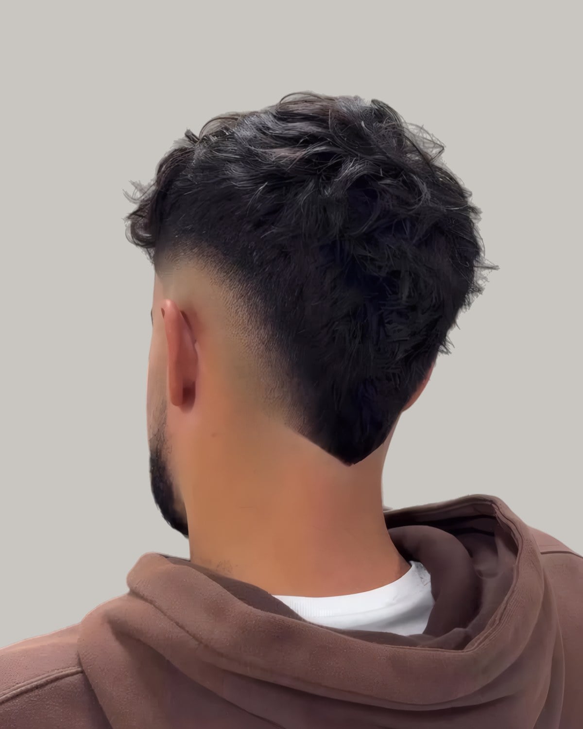 Man with a dark textured mullet and a burst fade, seen from behind at an angle