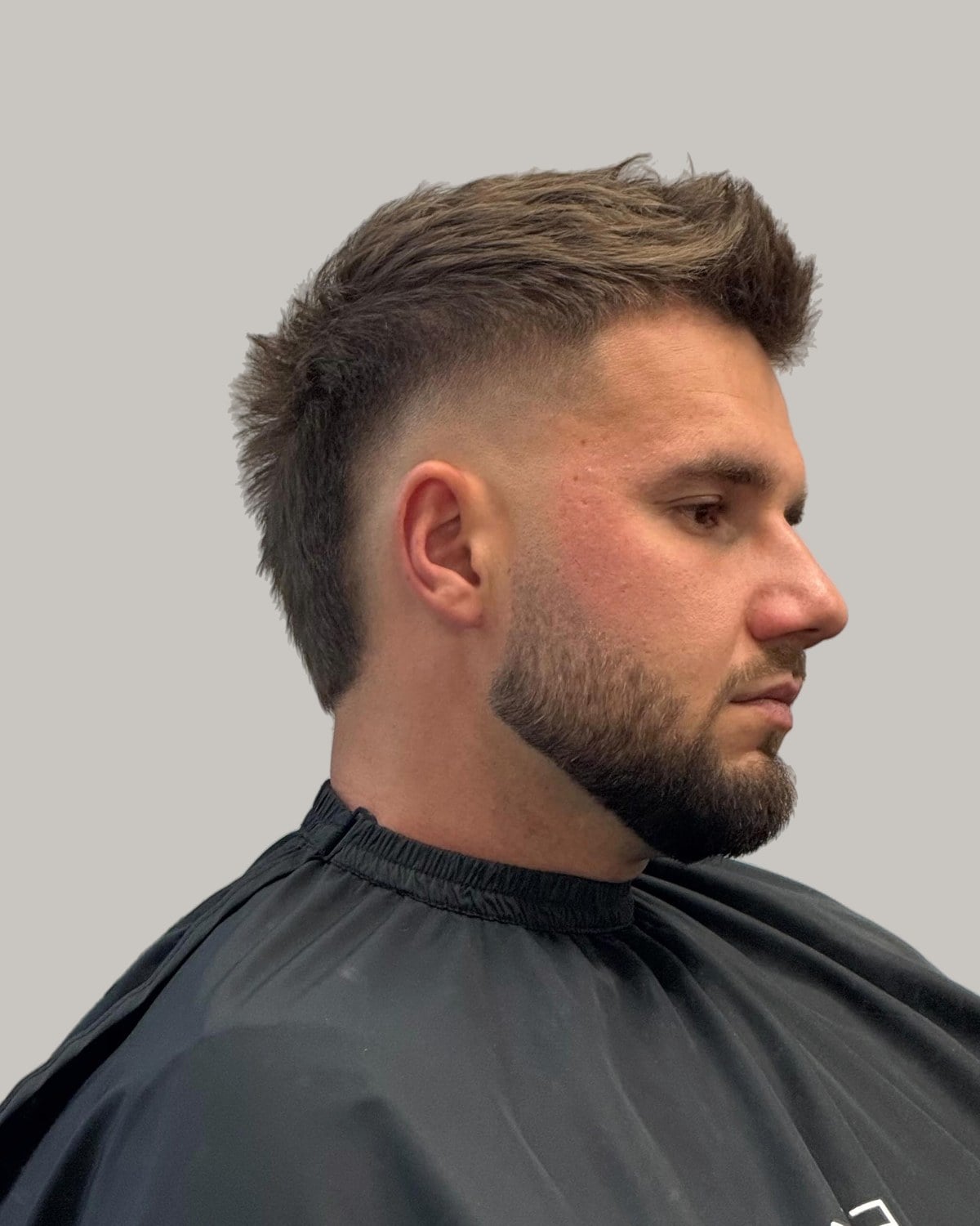 Bearded man with a light brown textured quiff and a burst fade, seen at an angle