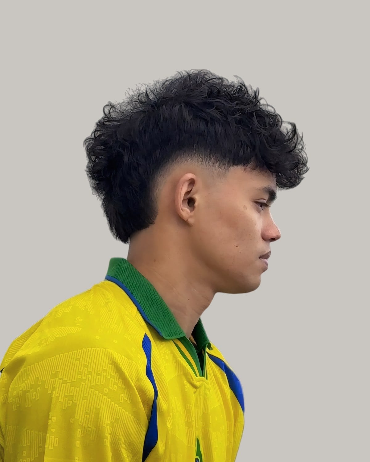 Young man with tight black curls and a burst fade, seen in profile