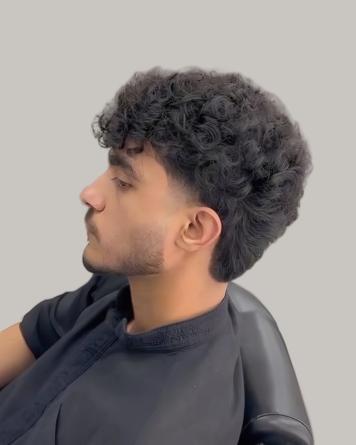 Man with tight black curls and a burst fade, seen from the side