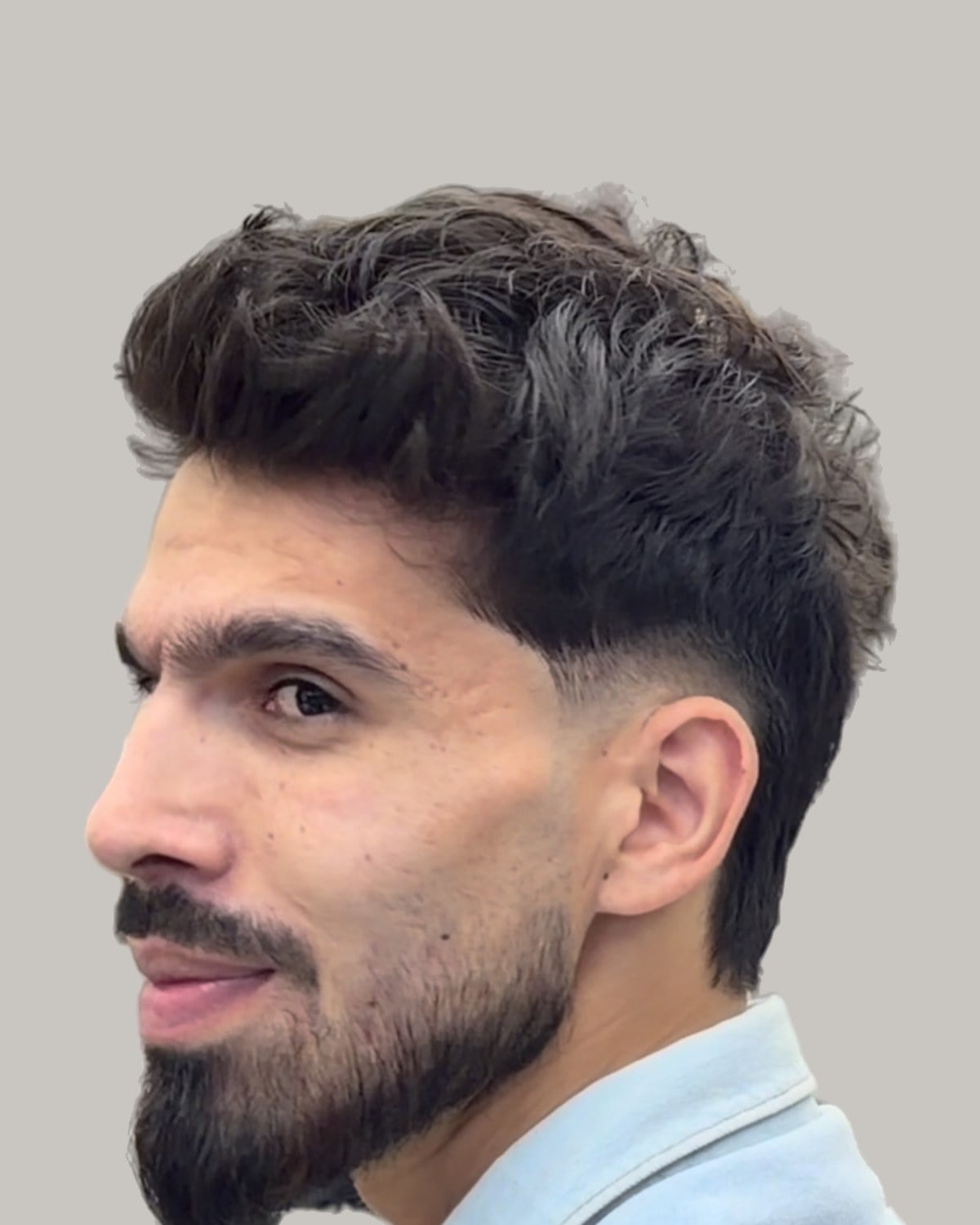 Smiling bearded man with a dark wavy crop and a burst fade, seen at an angle