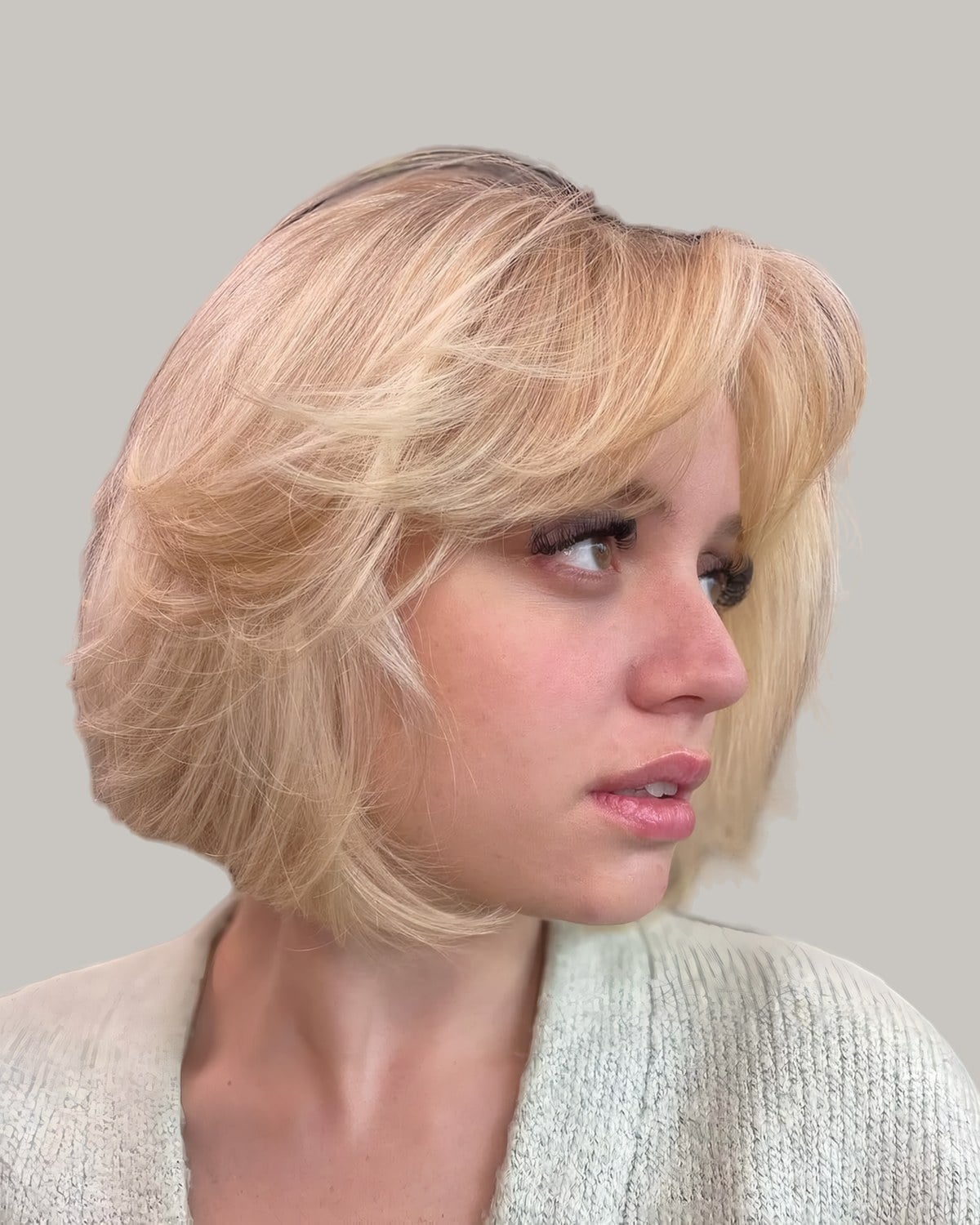 Woman in a cream cardigan with a pale blonde bob, bangs and flicked layers