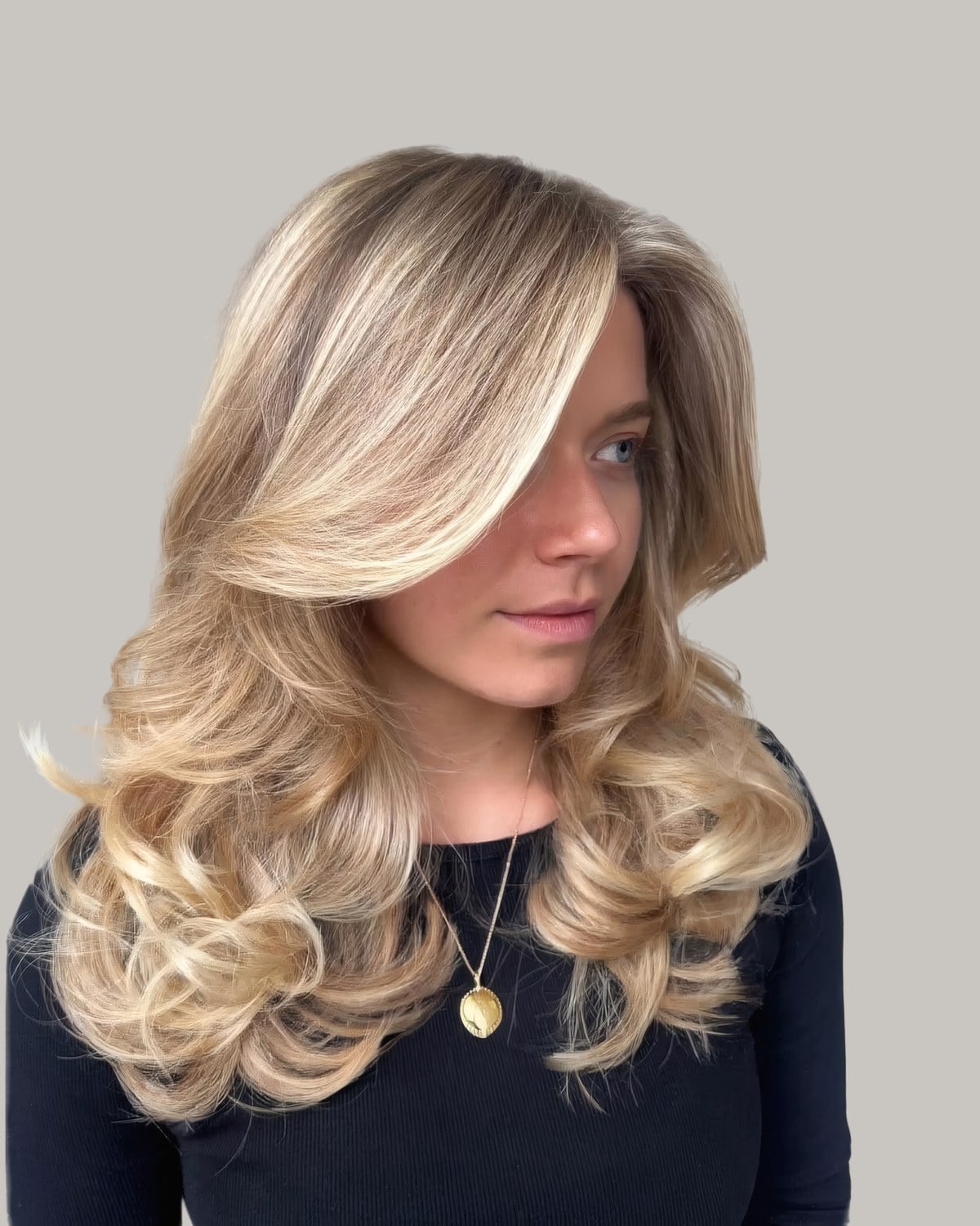 Woman with a blonde butterfly blowout seen from a three-quarter angle, the curls rolled outward