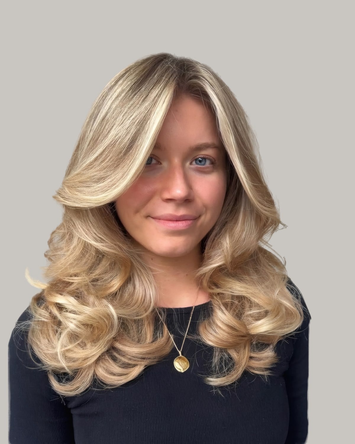 Woman in a black top with shoulder-length blonde hair blown out in big curls and swept-back front pieces