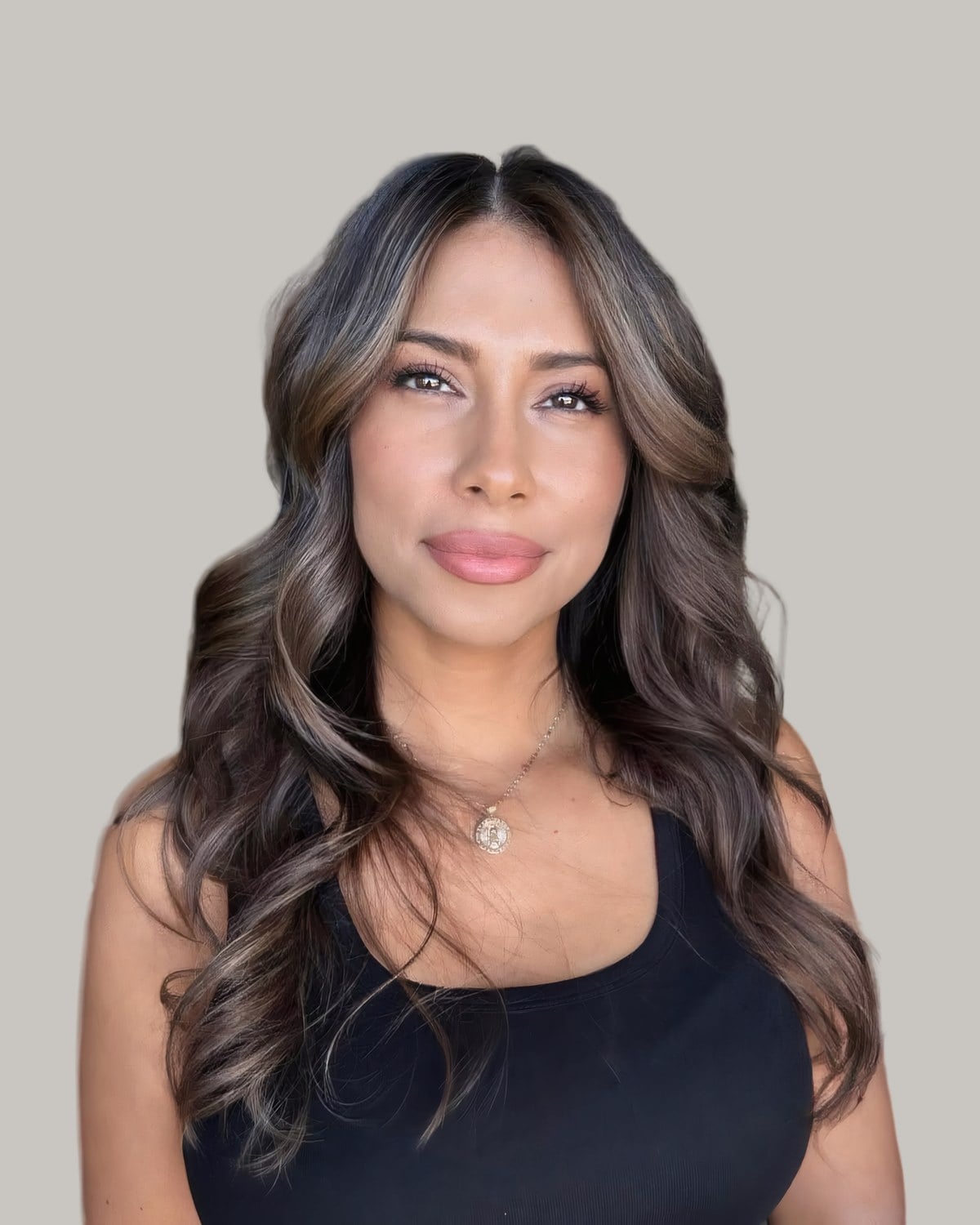 Woman in a black tank top with long brunette curls and babylights