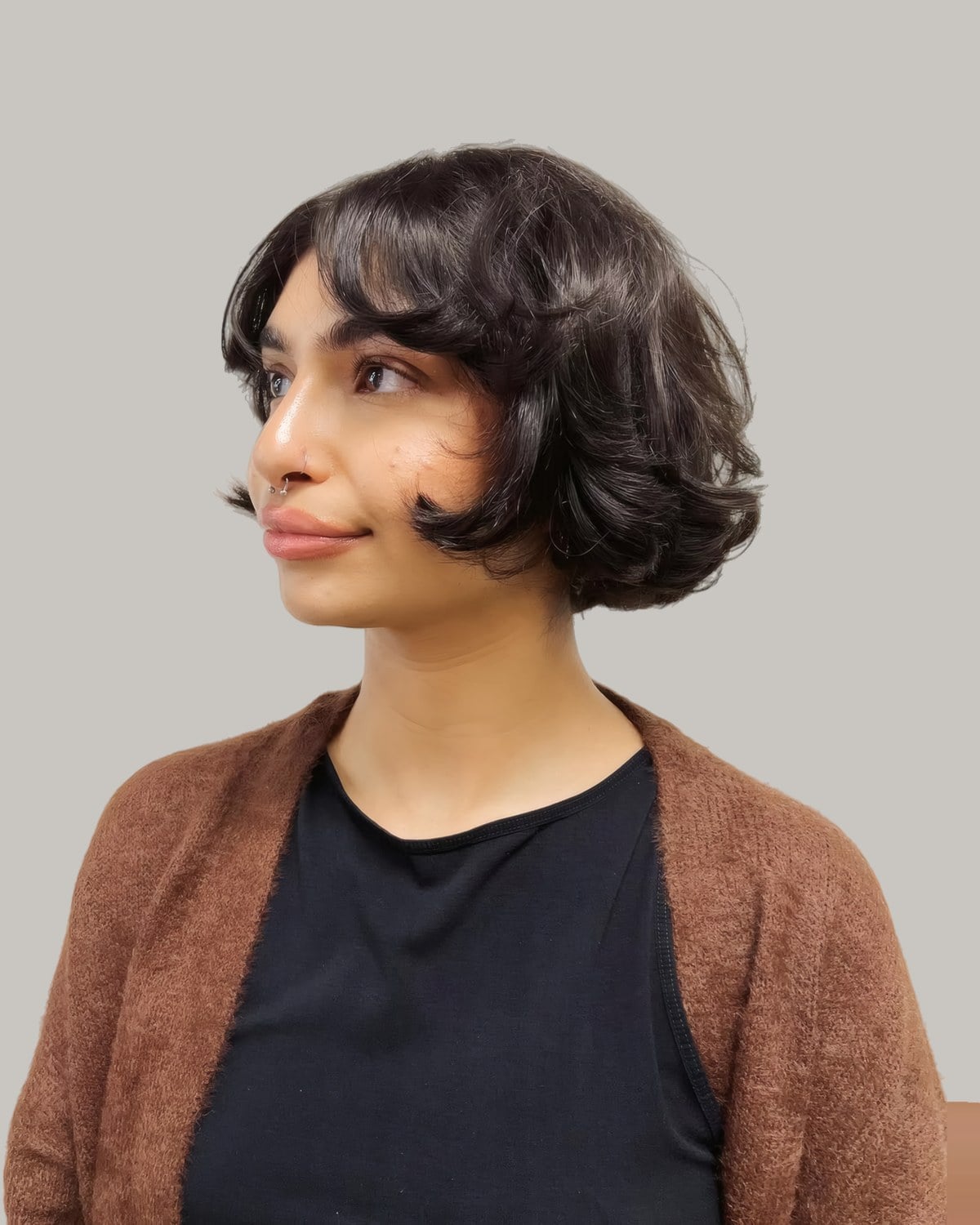 Woman in a brown cardigan with a short, wavy dark bob and bangs, seen from the side
